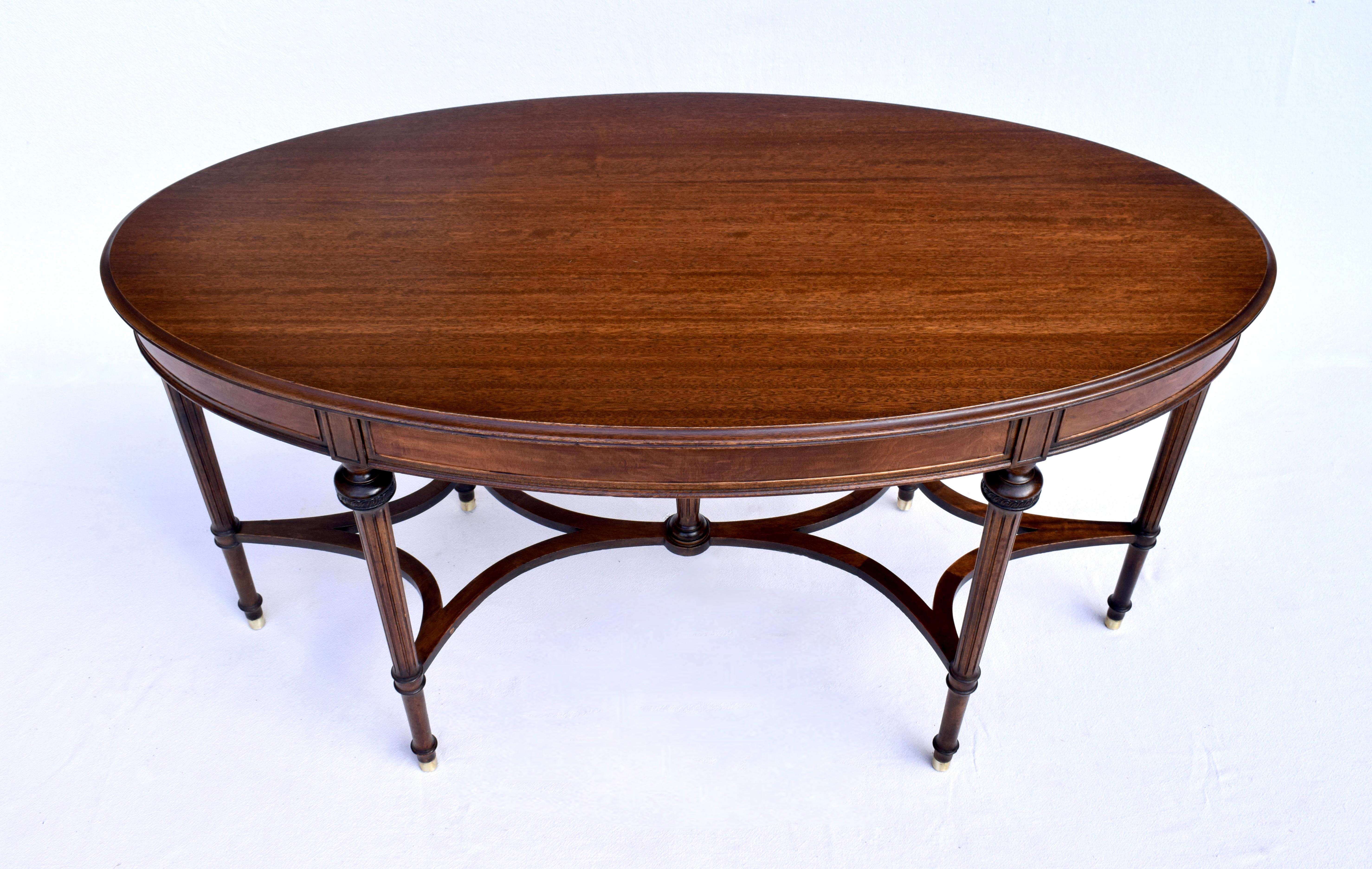 An exquisite Louis XVI style Mahogany oval table with a single hidden drawer, striking double reverse quatrefoil stretcher & six brass capped legs. Gorgeous grains with satinwood veneers on all sides the table renders marvelous multifunction,