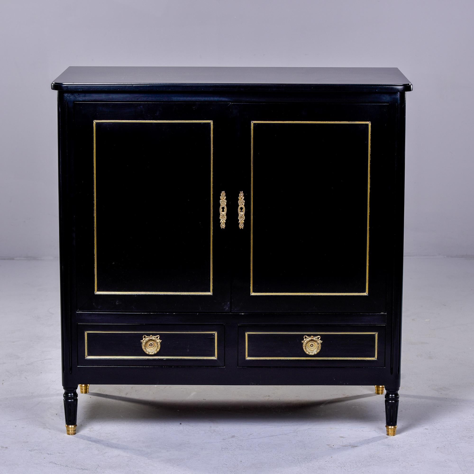 Circa 1910 Louis XVI style French mahogany side cabinet has a newly ebonised finish. Top compartment has two hinged doors with brass escutcheons, brass trim on the door fronts and a skeleton key. Below the compartment are two functional drawers with