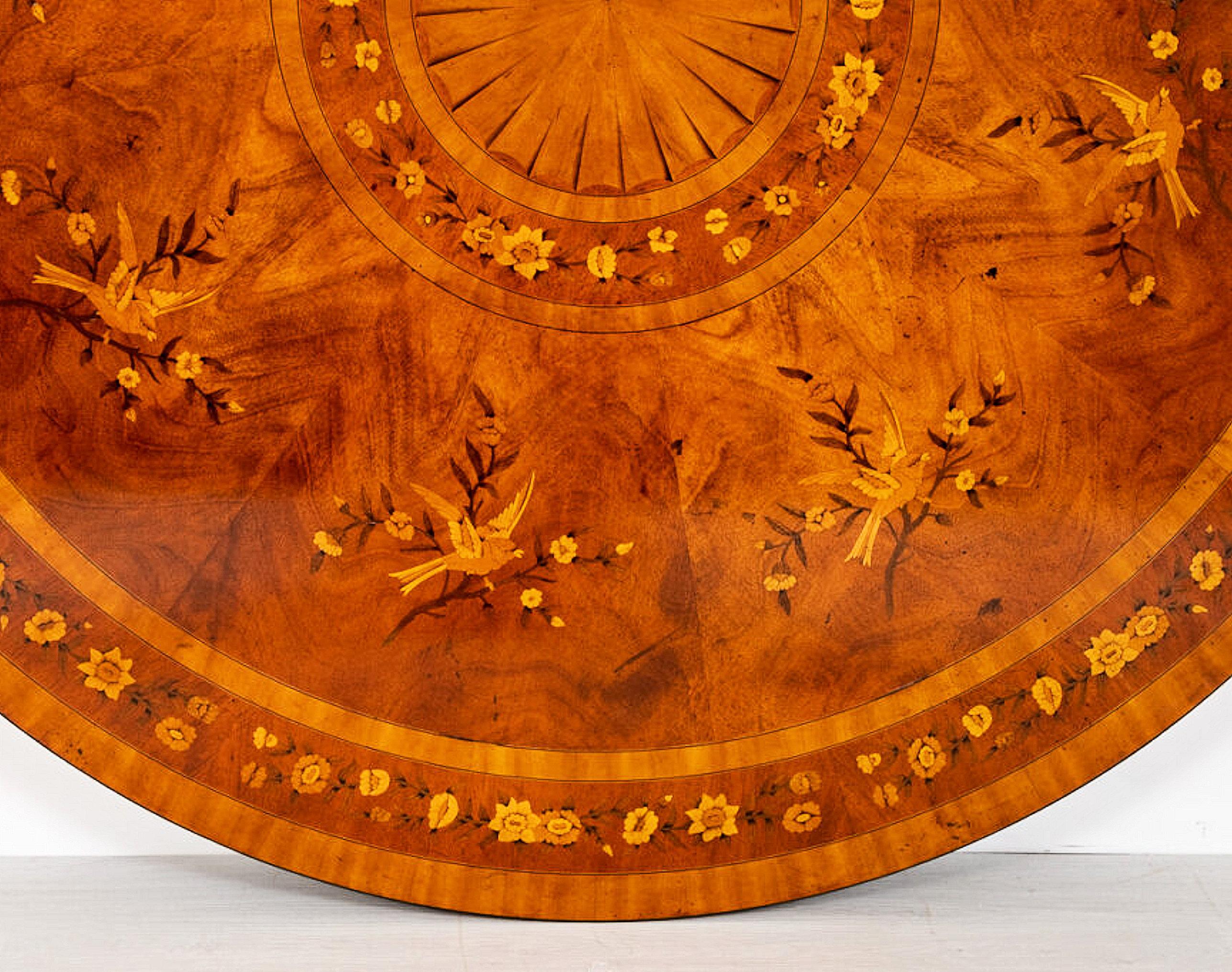 This superb quality and finely detailed mahogany marquetry dining table features a segmented centre circle with a banded and floral marquetry border and a bird motif around the center with another floral ring along the border edge. The border of the