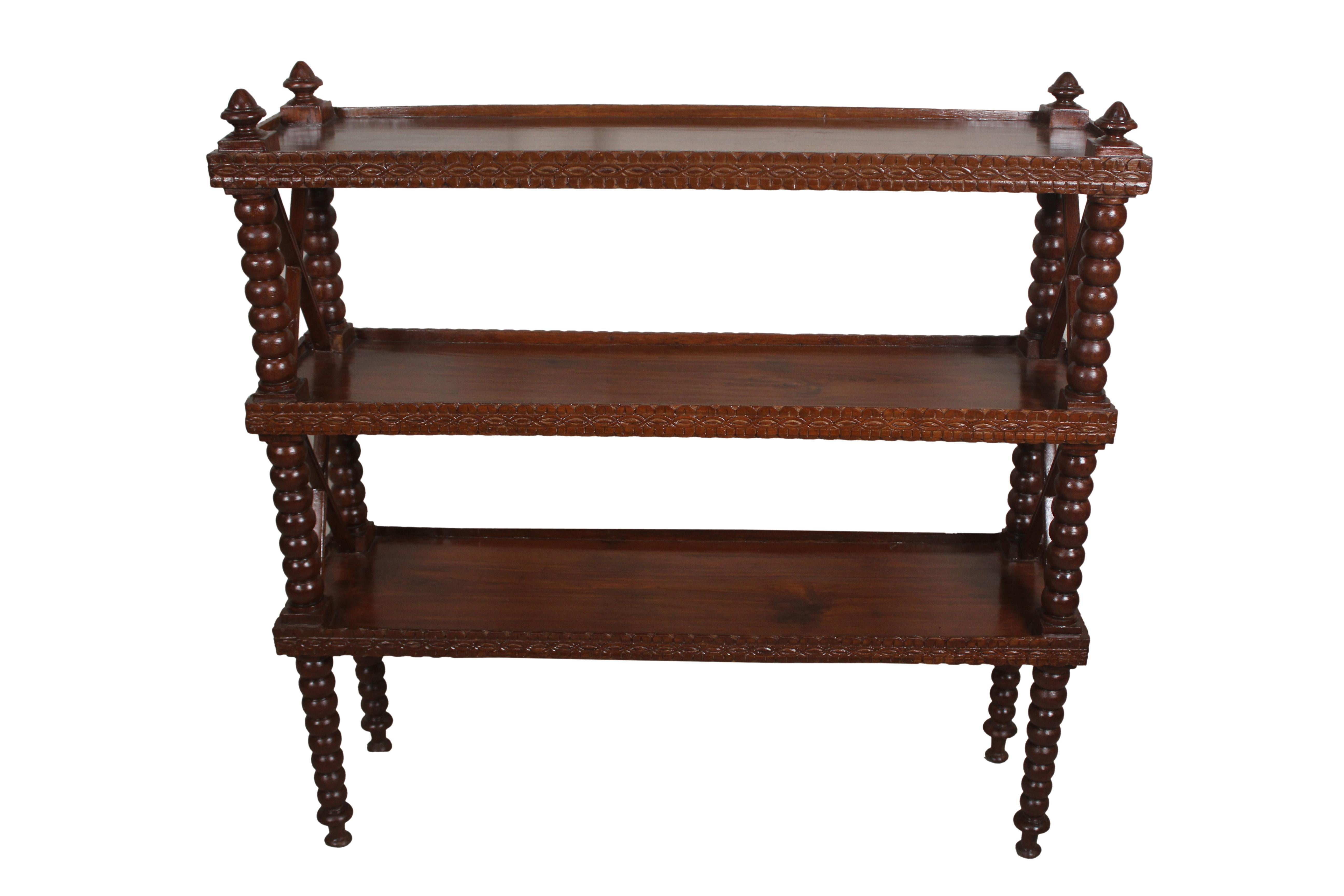 A large, three-tiered shelf, mahogany bookcase or étagère with hand turned bobbin spindles. Also carved fronts with a slight limp along all the edges keeping books and keepsakes from sliding off. Bobbins spindles are slightly tapered at the bottom,