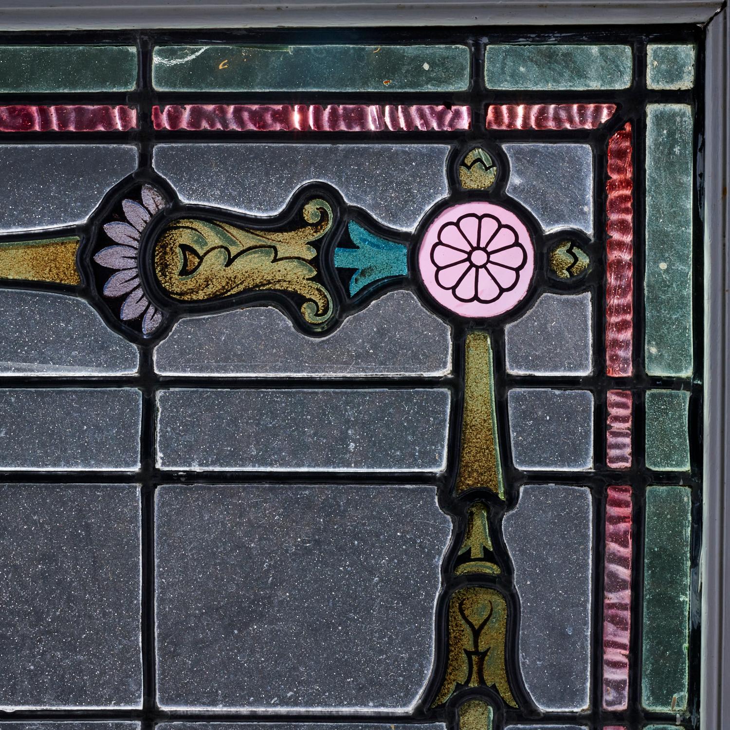 Early 20th c., a lovely pair of stained glass leaded windows in wood frames with hinges attached. The design could be interpreted in many ways. They could be considered to represent swords with hilts or a stylised floral trellis. The pink floral