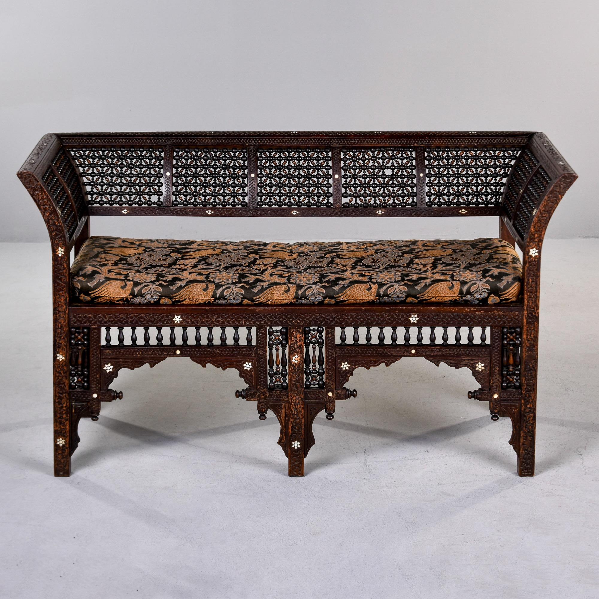 Found in Turkey, this hand-carved wood settee dates from approximately 1910. This backrest and sides of this settee feature an intricately carved lattice pattern with no breaks or repairs found. The settee frame is adorned with white shell inlay and