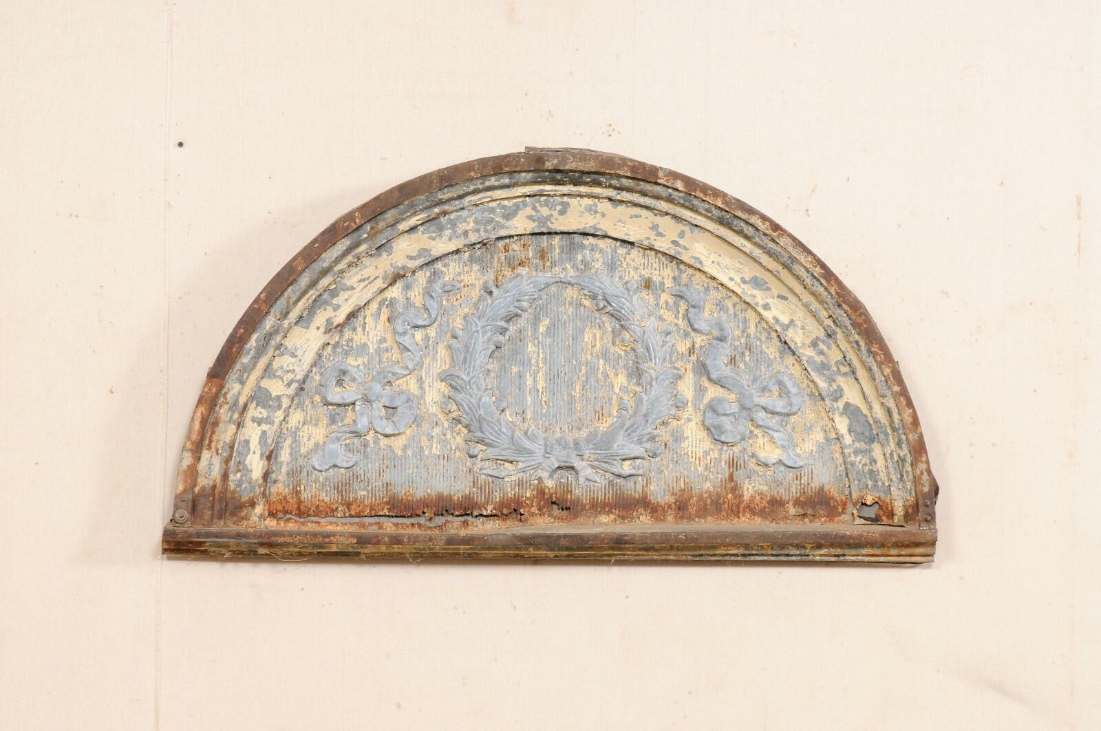 An American zinc arched pediment from the early 20th century. This antique architectural piece from American has been designed with Neoclassical inspired wreath and ribbon bow-ties within its center and has a half-moon, arched shape with flattened