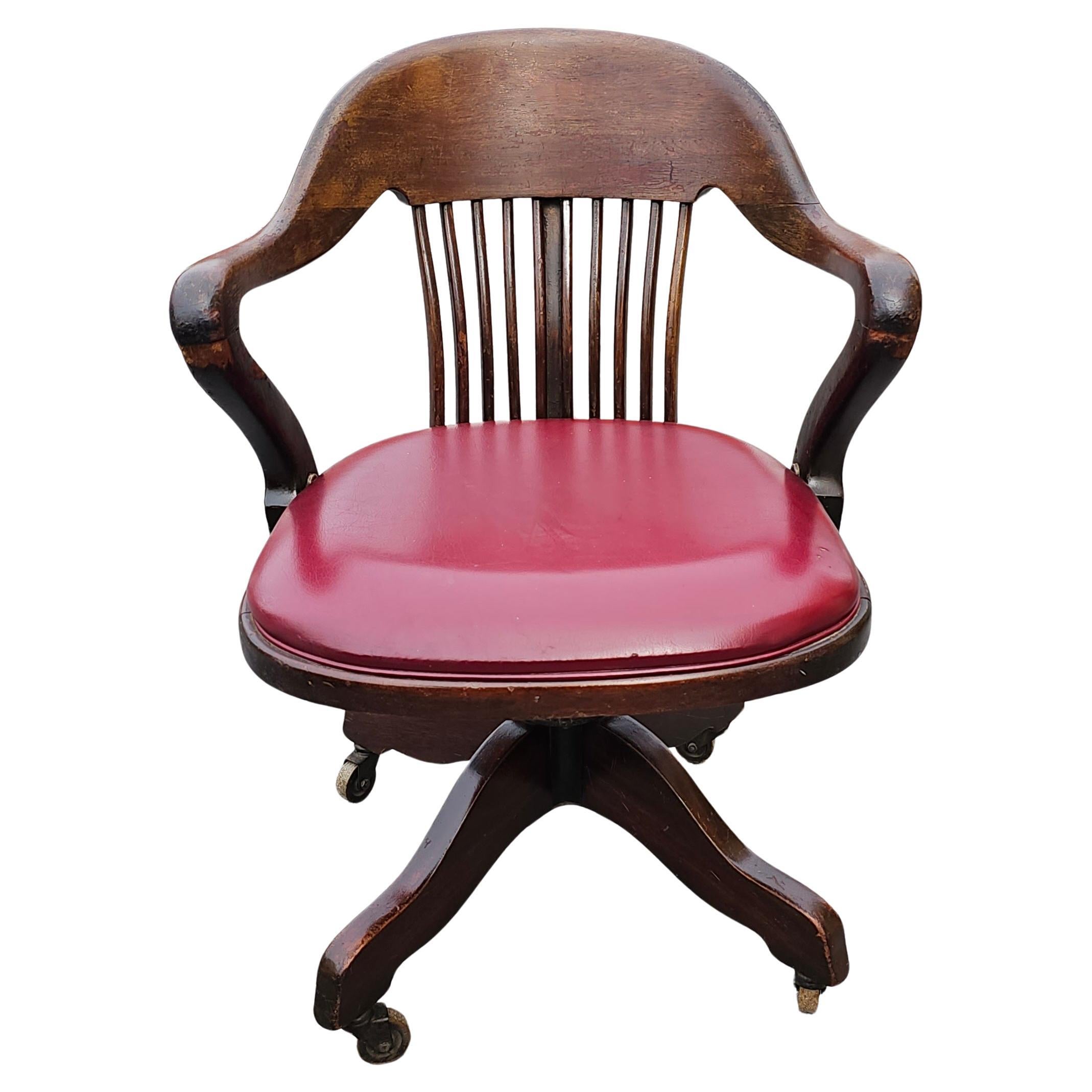 Chaise de banquier du début du 20e siècle en chêne et assise tapissée de vinyle, à roulettes, basculante et pivotante. Mesure 23,5