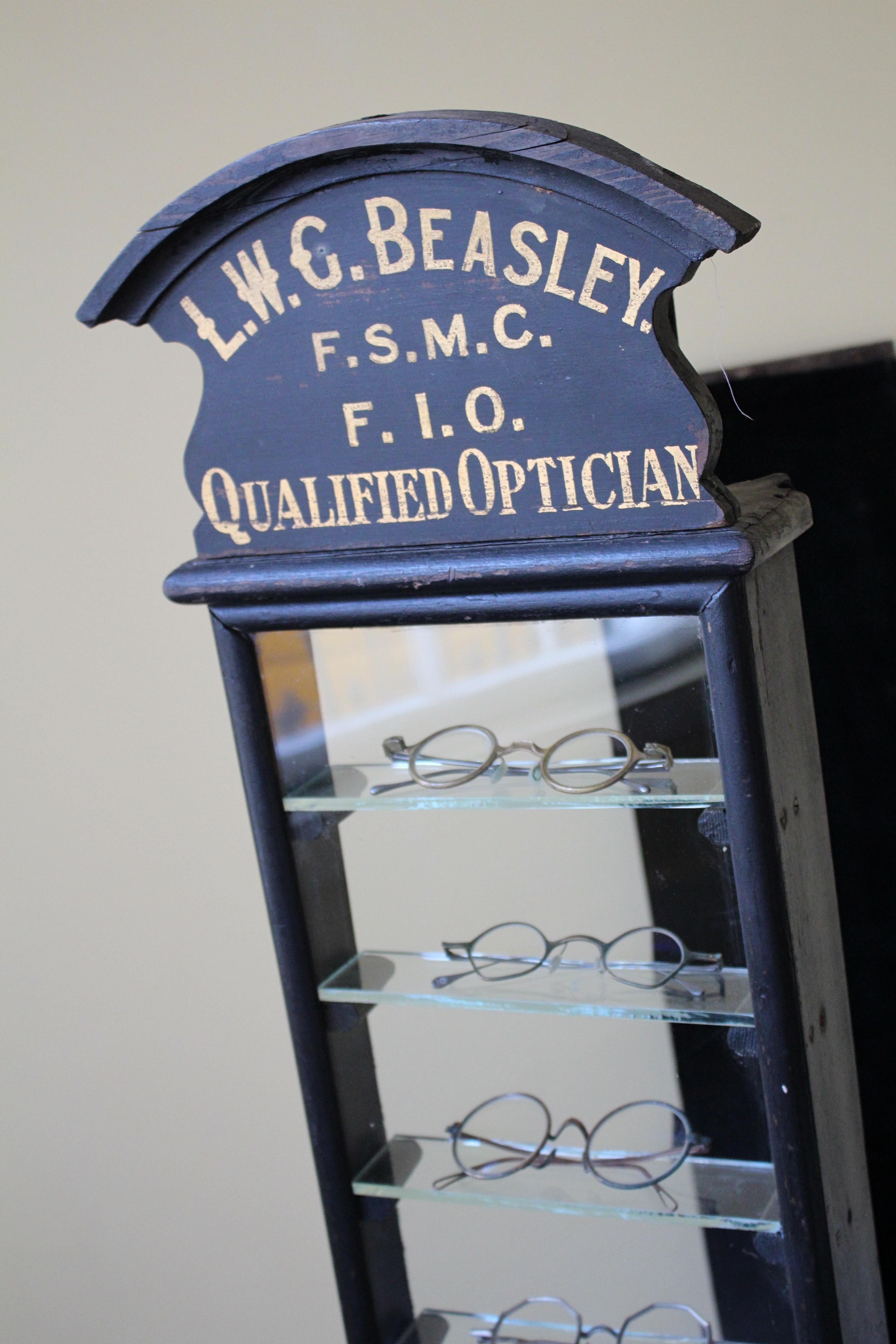 An early 20th century opticians display cabinet, with its original hand painted gilt advertising signage over a decorative pelmet.

Lead lined outer top, so one would assume was previously used outside. Iron hanging brackets, and its original worn