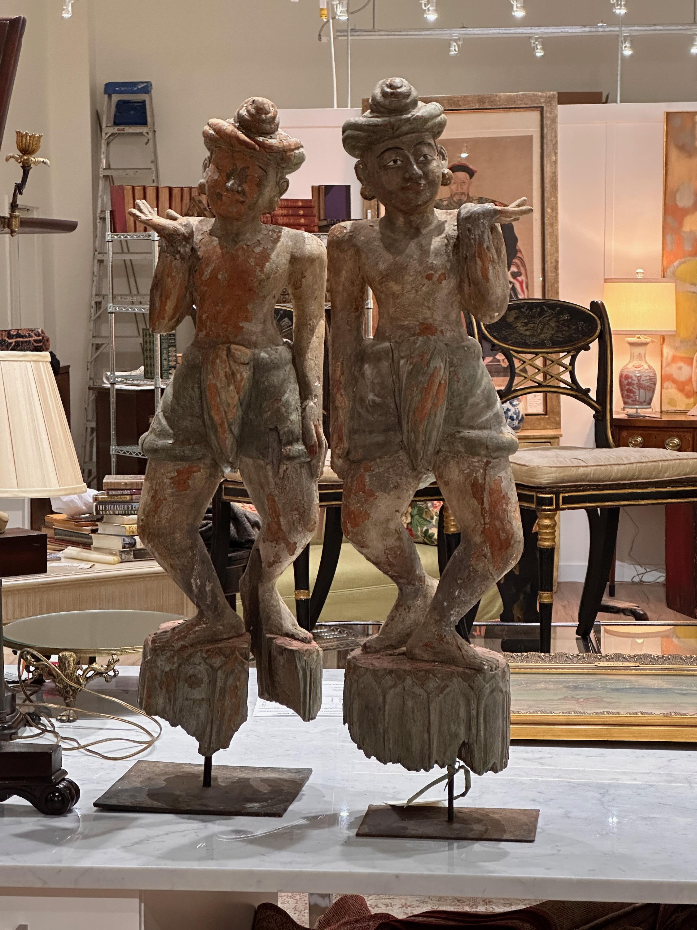 A pair of early 20th C. carved wood and polychrome decorated Indonesian standing figures in mirror image on metal bases.