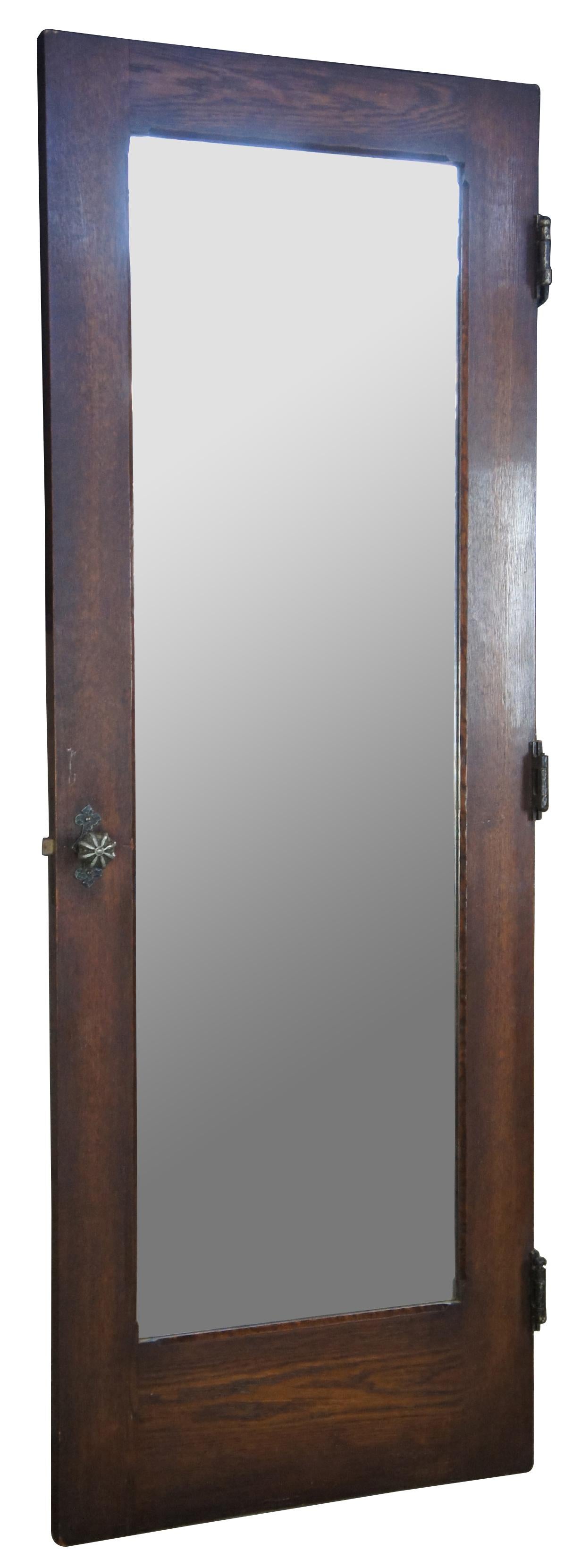 Early 20th century oak door. Features a large central mirror and Spanish Revival hammered hardware. Reclaimed from one of the first homes built in oakwood, Ohio by Harry I Schenck, circa early 1900s. Great for use as a dressing mirror. 5 available.