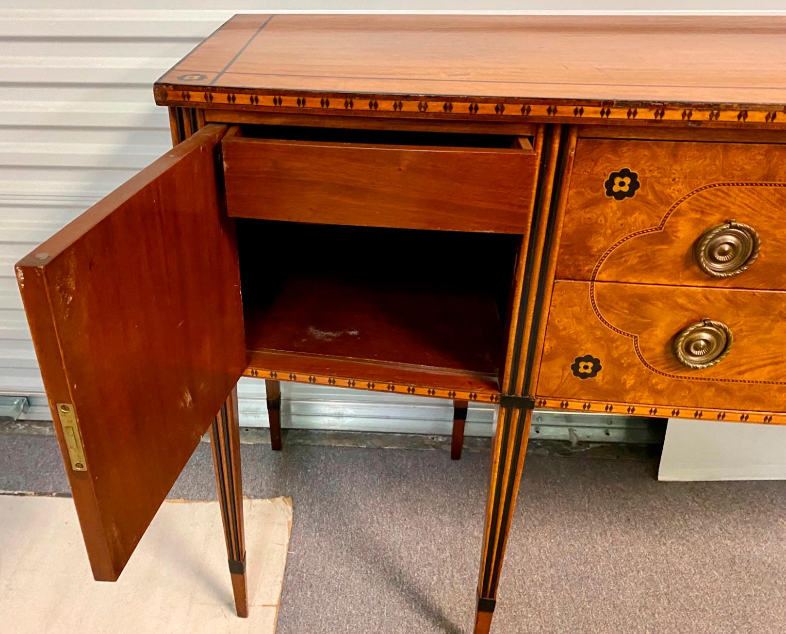 This is a wonderful piece. It is an early 20th century Robert Irwin for Royal Furniture sideboard. It has both satinwood and ebonized inlay. It is marked in the drawer and includes the keys. The long, tapered legs are also inlaid.
