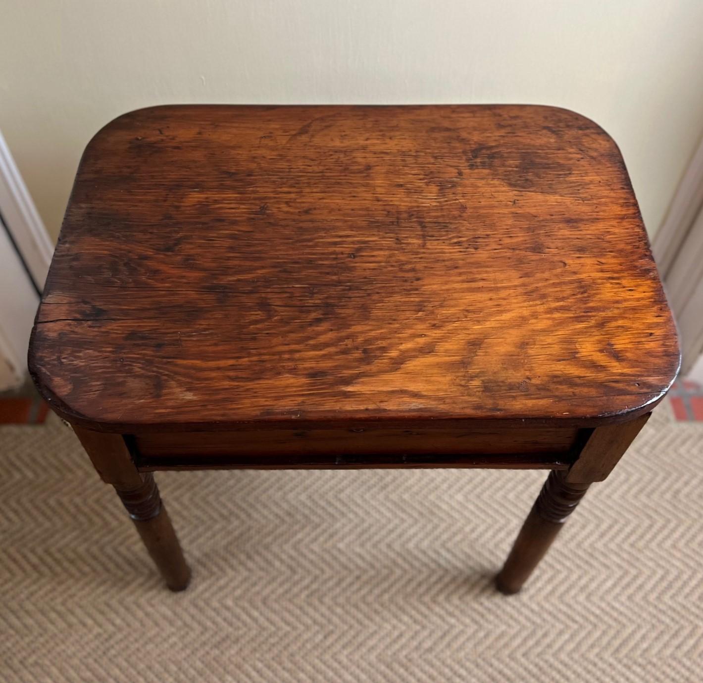 Likely early 20th C., a sweet, rustic and honest side table with lockable drawer (key not retained). The table top is made of a single slab of wood with rounded corners on turned bobbin legs. The table shows evidence of use and care over many years