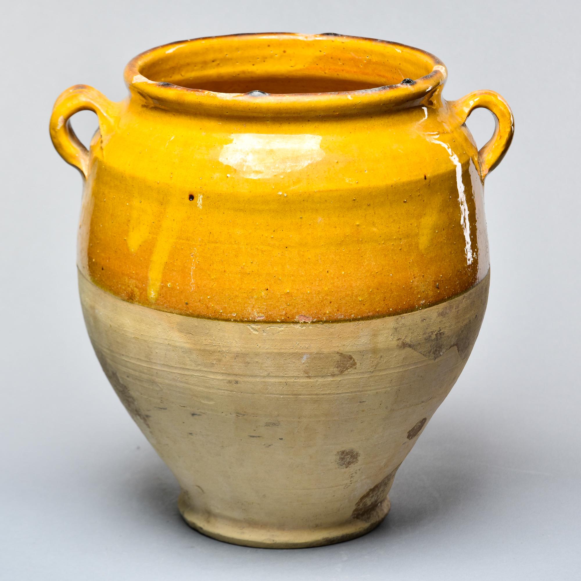 Found in France, this French confit jar dates from approximately 1915. This piece stands 12.25” high and has the traditional form with a wide vessel body and two handles on the sides with a mustard-colored glaze on the outside top half and fully
