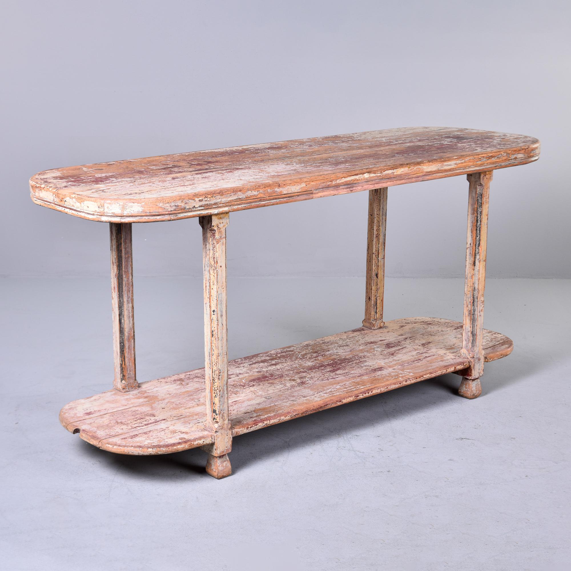 Found in France, this circa 1900 two tier table has an elongated oval top and lower tier with four legs and remnants of the original painted finish. Original paint of deep red and creamy antique white is mostly worn away and has been sanded smooth