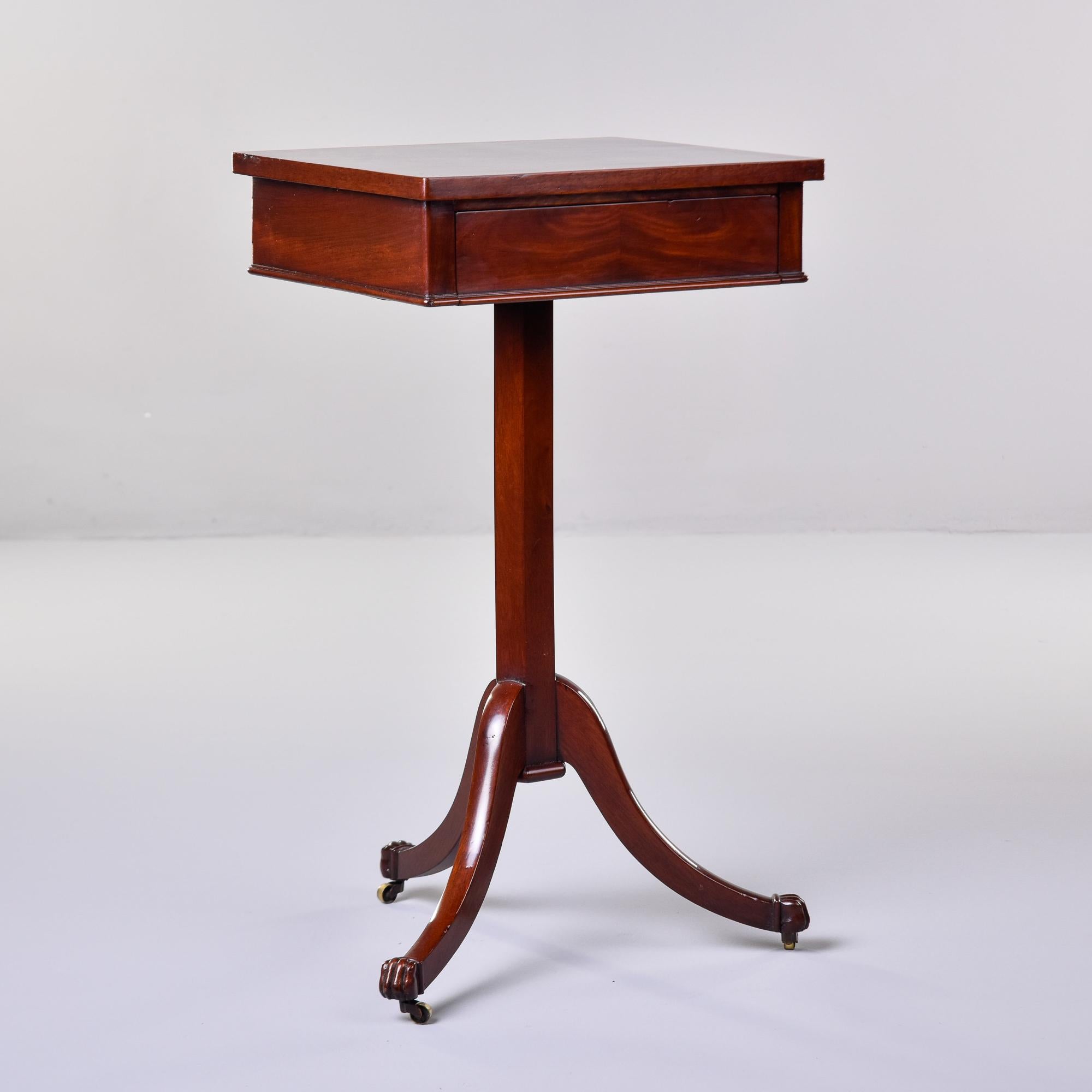 Found in England, this mahogany side table dates from about 1920. Tripod base has curved legs with original brass casters and paw feet. Six-sided center support with a table top an inch shy of being an actual square and one functional drawer. Nicely