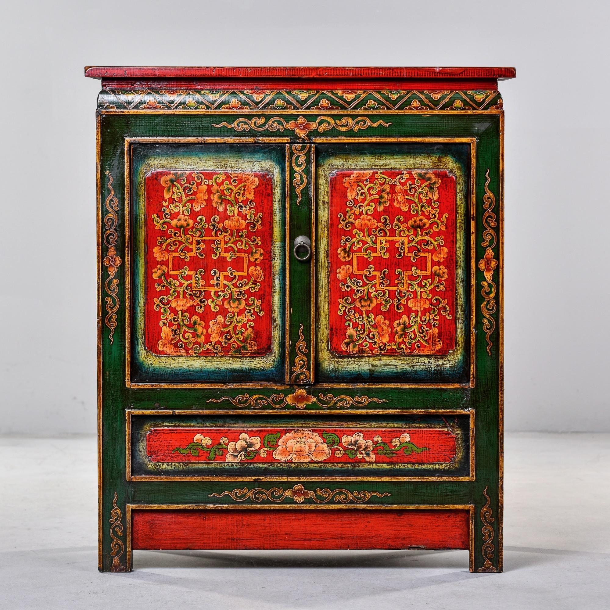 Circa 1920 Tibetan cabinet in vibrant shades of red and green. Hand painted floral and lattice details on front, sides and top. Two front doors open to storage with a single internal shelf. Unknown maker. Very good antique condition with minor