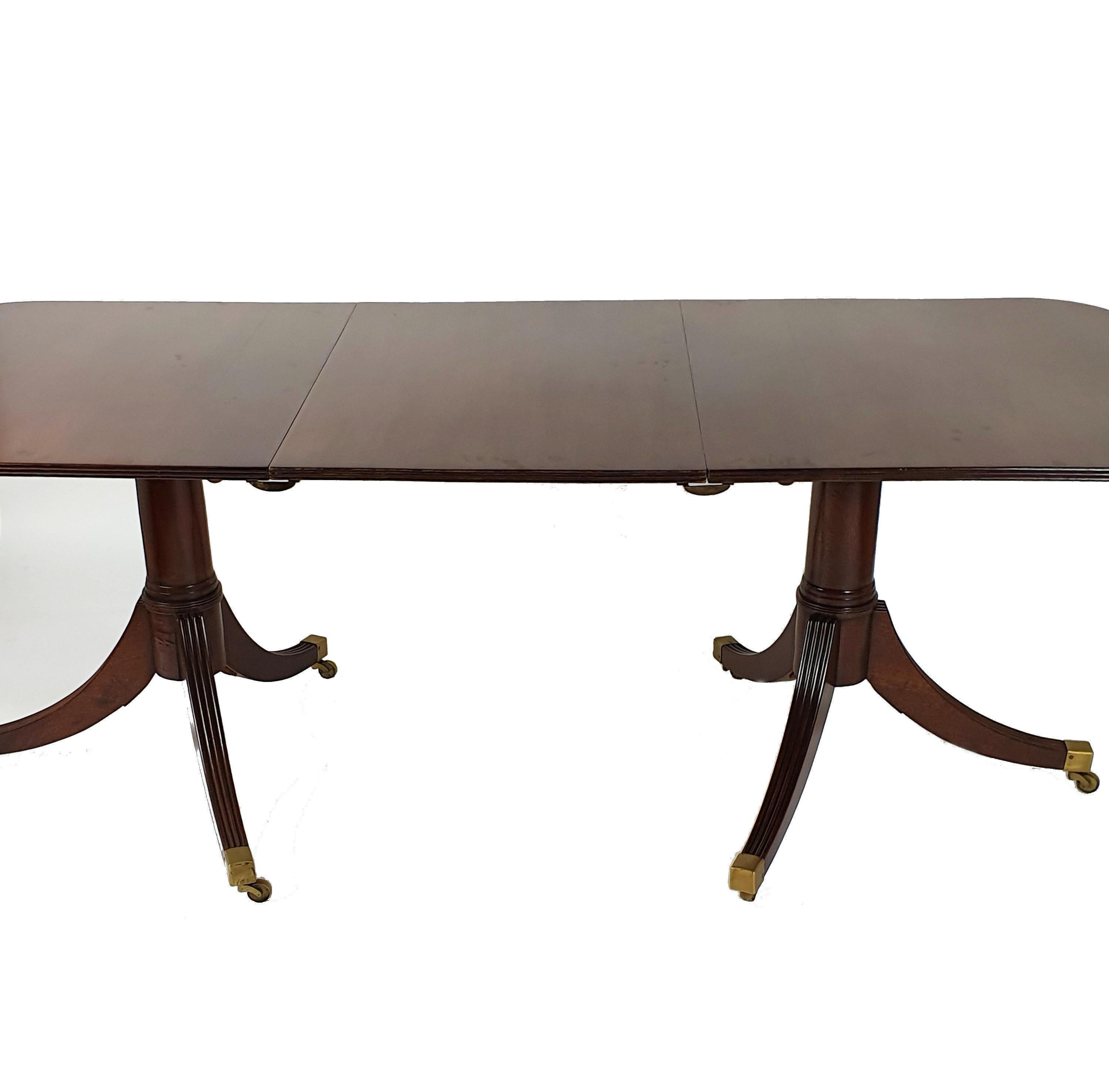 This very attractive and well-proportioned mahogany dining table has a lovely patina top and stands on twin pedestal tri pod legs with one central removable leaf. The table ends and the leaf attach together with brass clips, as well as having brass