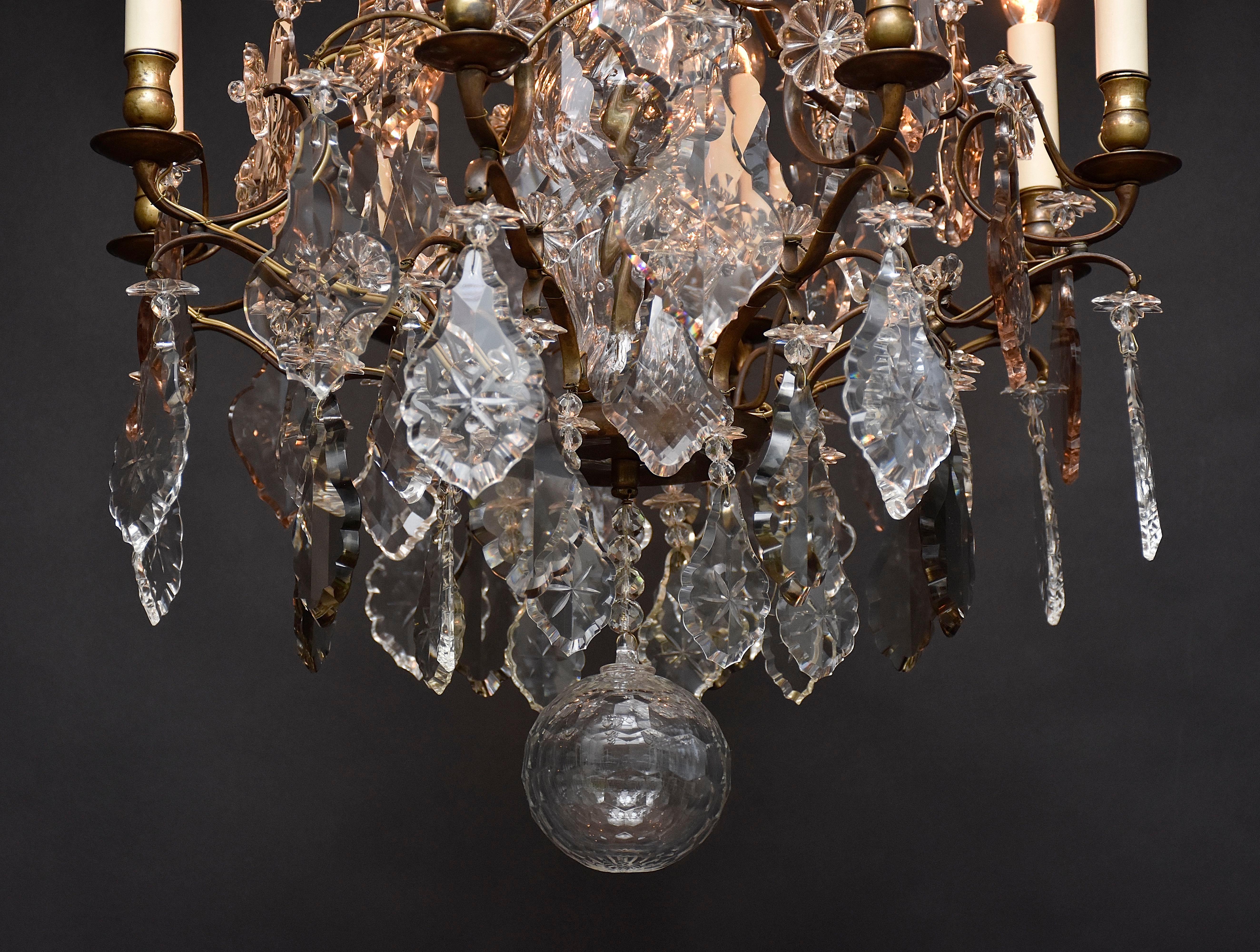 Ein sehr eleganter Kronleuchter im Rokoko-Stil mit 8 Lichtern.
Der Kronleuchter ist reich verziert mit schönen großen geschliffenen Kristallpendeln, Blumenrosetten und Sternen. Einige der Kristalle sind zart gefärbt.
Der zentrale Schaft ist mit