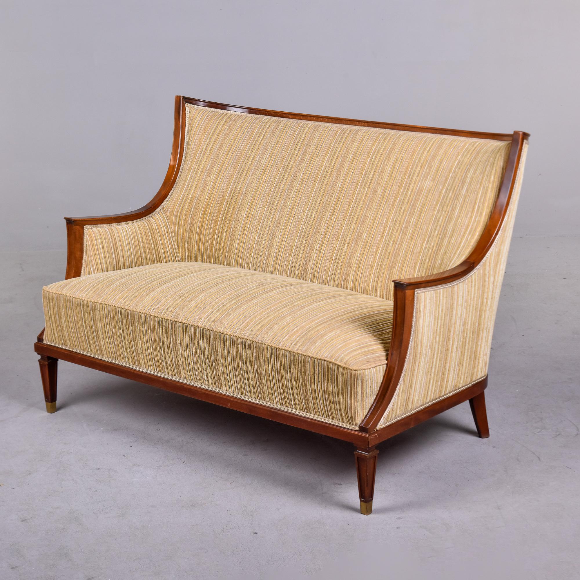 Circa 1930s small Swedish sofa with walnut frame, tall back and brass capped front legs. Sleek lines with curves and high backrest. Very solid piece with hardwood frame and spring construction. Pale gold striped chenille upholstery is in good