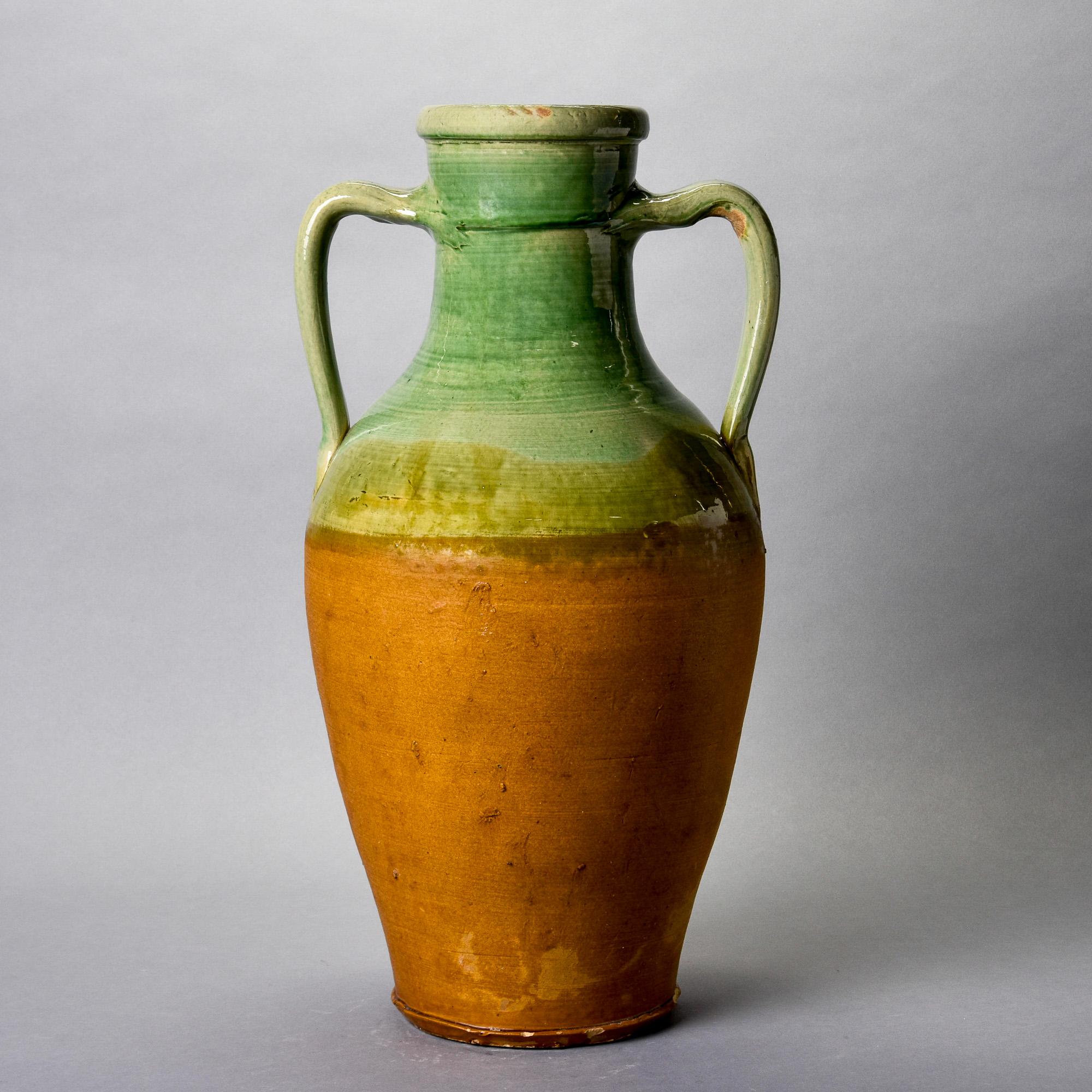 Found in France, this large amphora-shaped vase dates from approximately 1910. Glazed in traditional French colors with warm brown glaze at the base and green glaze on the handles and neck. Unknown maker. Some visible age-related surface wear