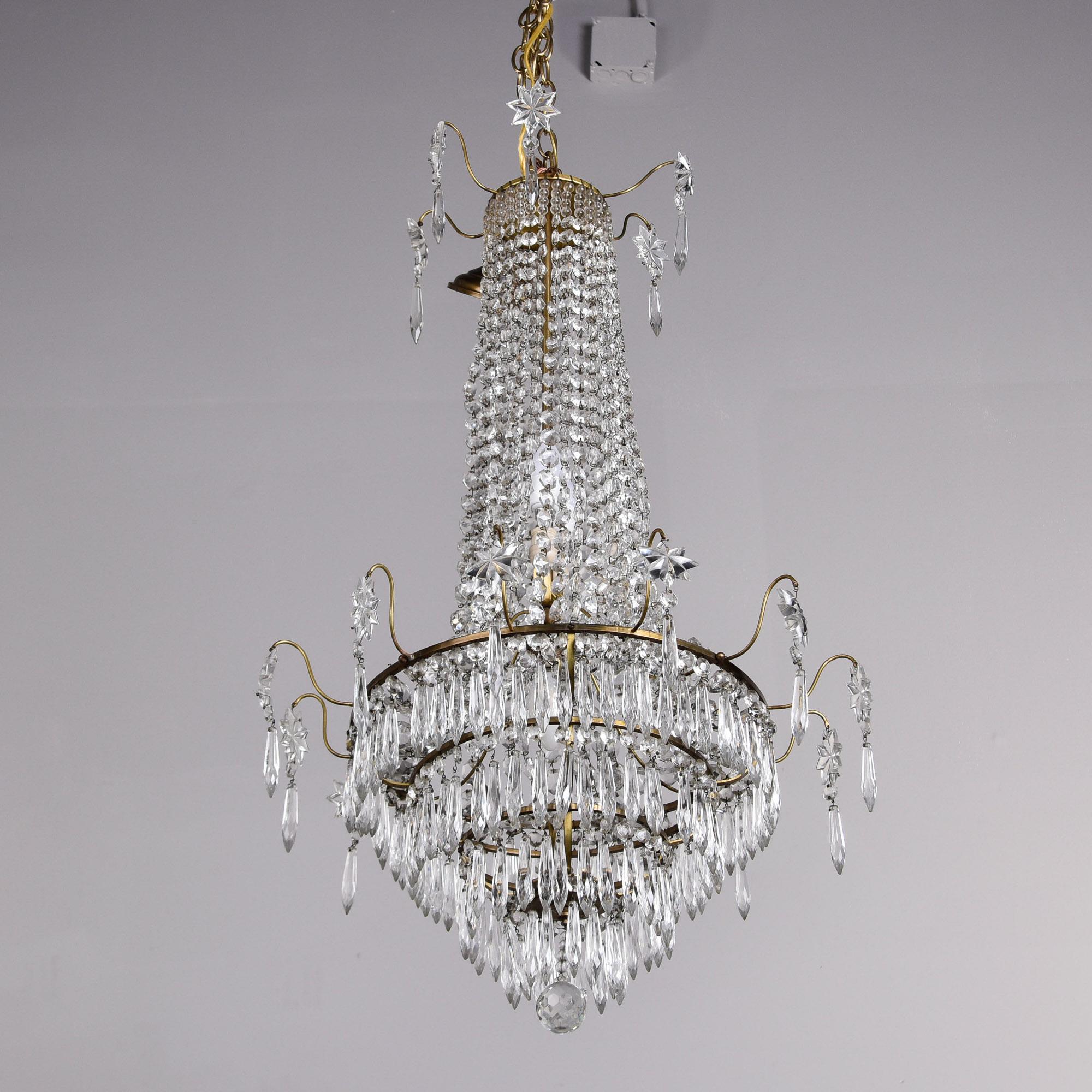 Questo lampadario in cristallo svedese del 1900 circa è alto 35 pollici e ha un diametro di poco inferiore ai 20 pollici. Il lampadario con cornice in ottone è caratterizzato da quattro livelli a cascata di pendenti a lancia di cristallo