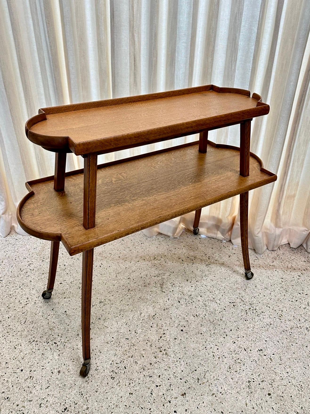 This is a RARE two-tier oak table with tray edges and tapering legs on casters.   This elegant and beautiful table shows its rich history and would be perfect for display or serving desserts, cheeses and tea/coffee, liquor bar service.