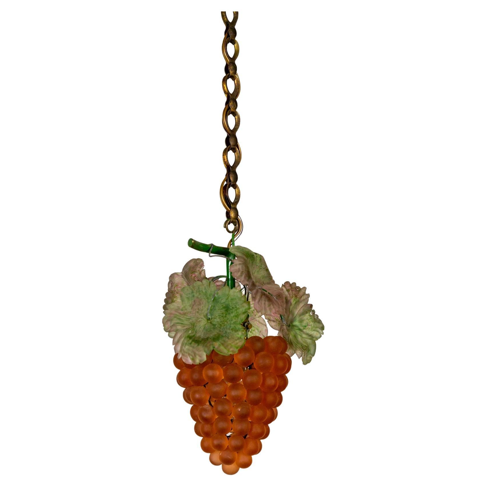 A vibrant pendant light from the 1920s; ruddy-red to amber, Venetian glass grape bunches with detailed green and pink leaves. The grapes are hanging from a green, patinated brass 