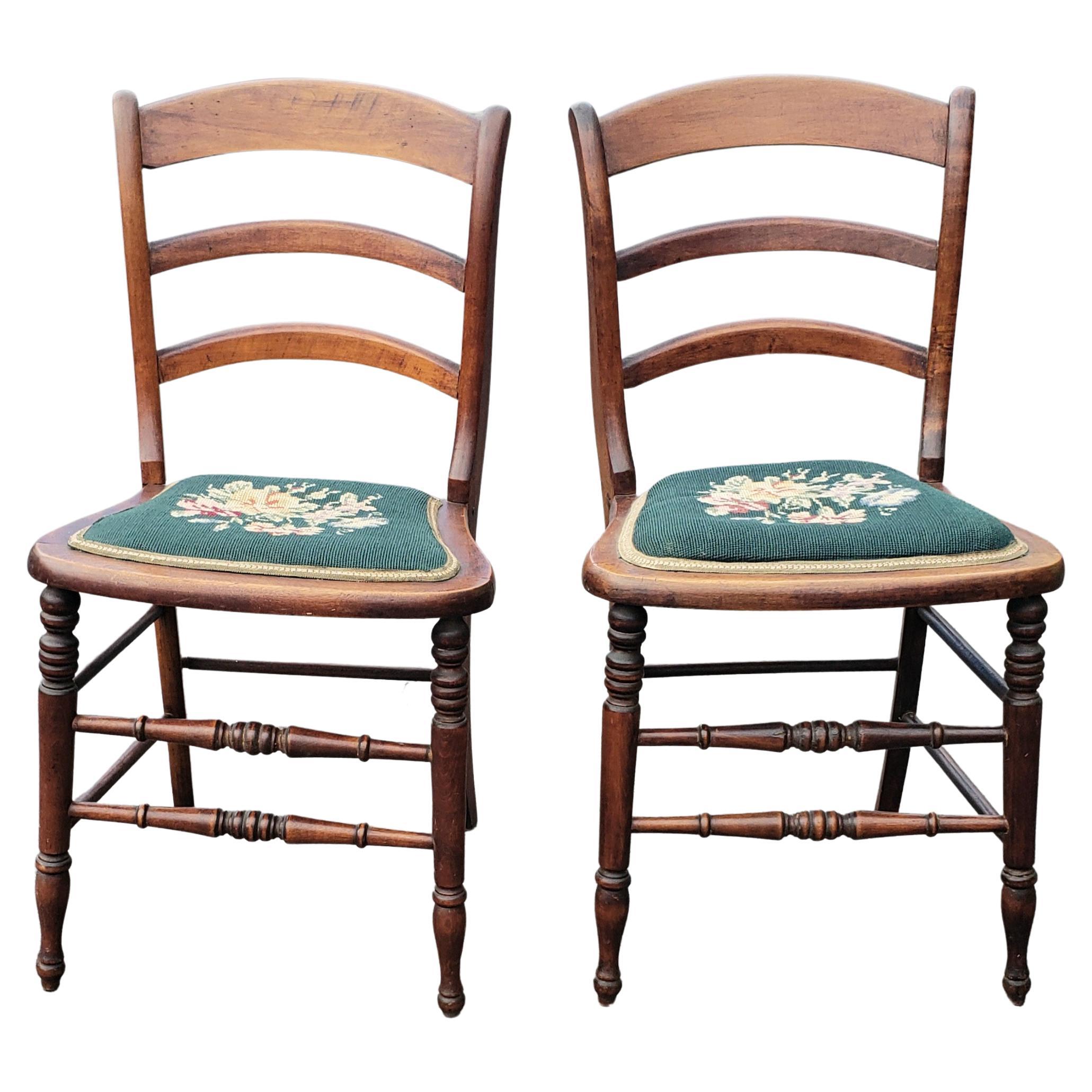 A pair of early 20th century Victorian style ladder back walnut and Needlepoint upholstered seat side chairs in very good vintage condition.