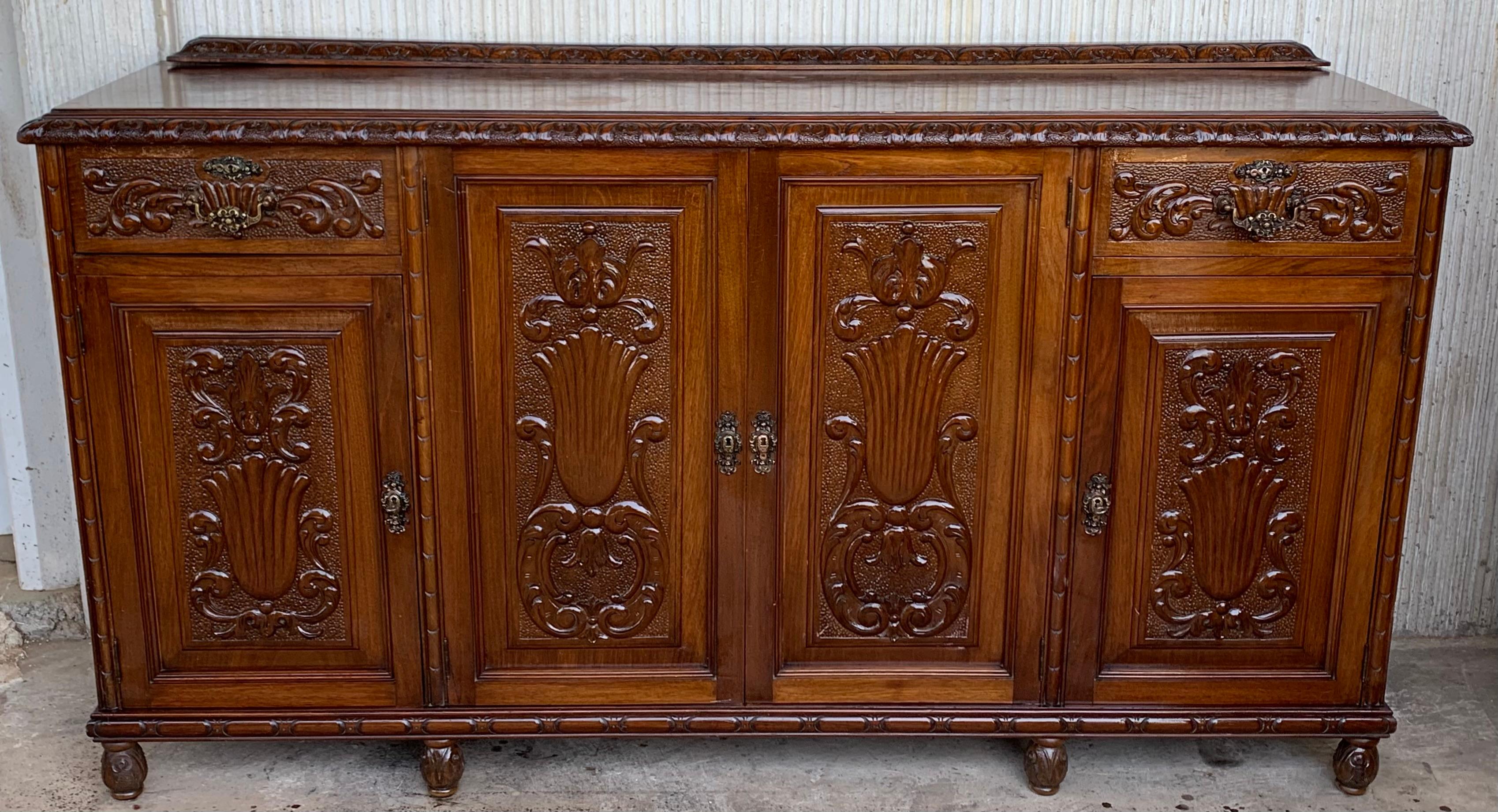 Early 20th carved walnut sideboard with four doors and two drawers
Elaborate carved walnut sideboard from Spain is topped with a wood top. Two dove-tailed drawers are accented with bronze hardware. Four doors open for ample storage. The shelves on