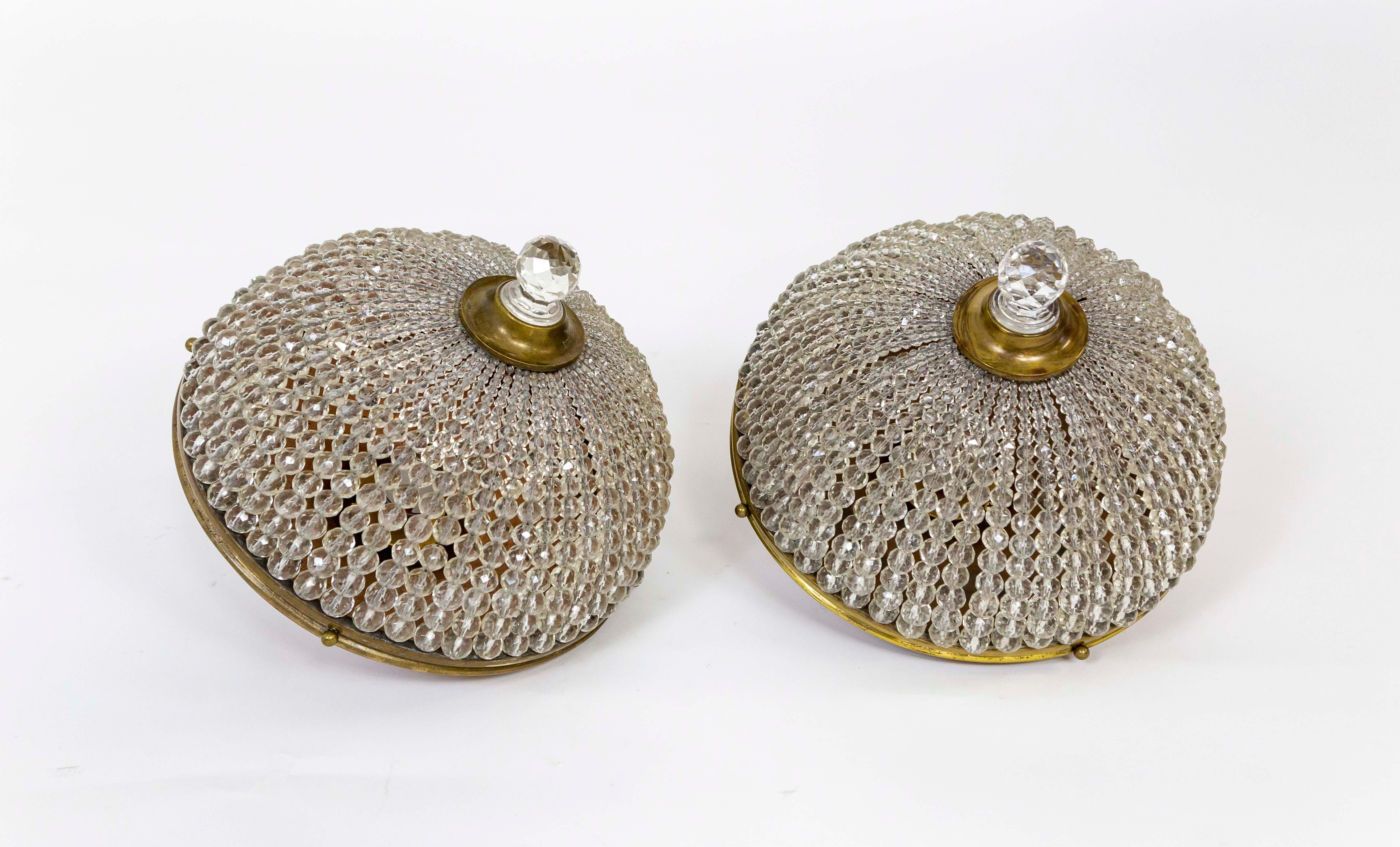 A pair of light fixtures created with Czech crystals strung on tightly-knit wires from a brass rim forming half-spheres. The shades are held with copper flush mounts and capped with brass and large crystal finials in the centers. Early 20th century.