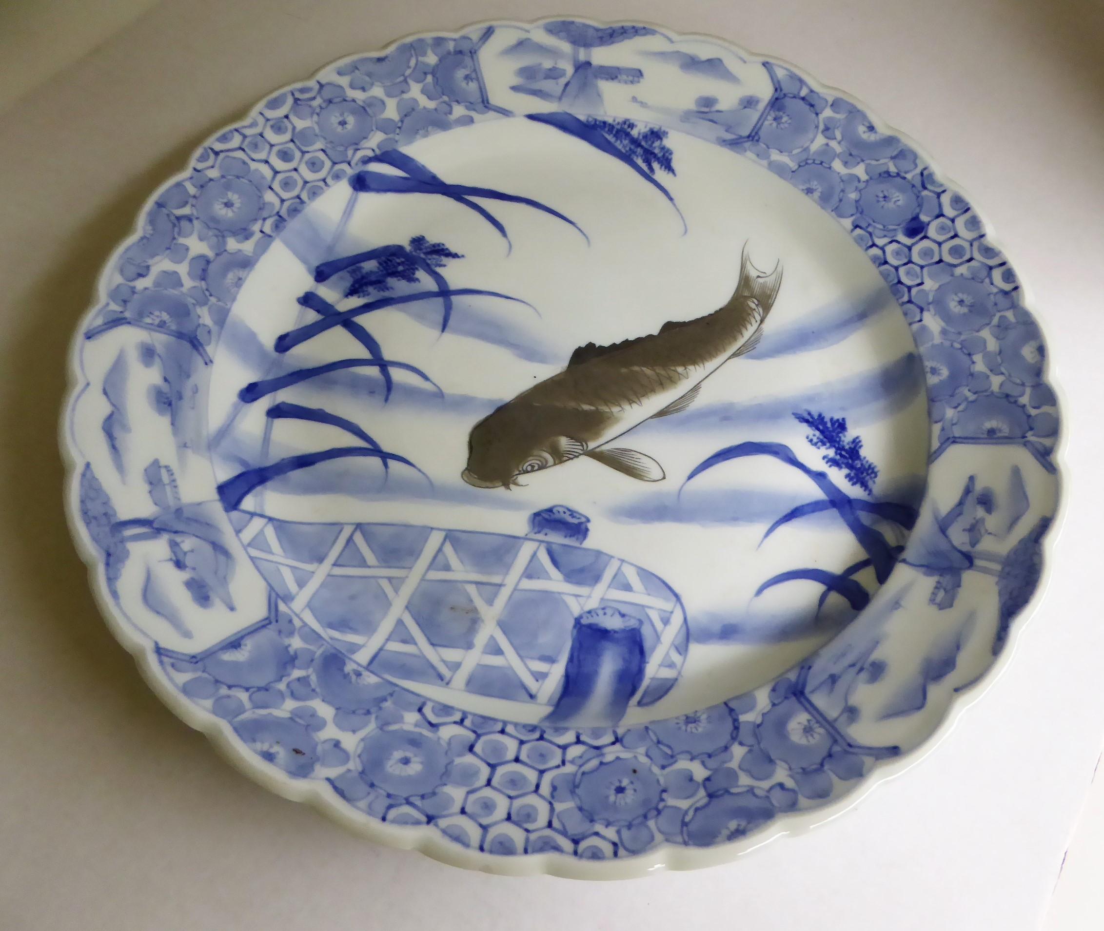 Beautiful and unusual blue and white antique Japanese Imari Charger depicting a dark colored Koi swimming among the reeds close to a stylized pier, early 20th century. Appropriate firing marks centered on back and underglaze Japanese mark. Very good