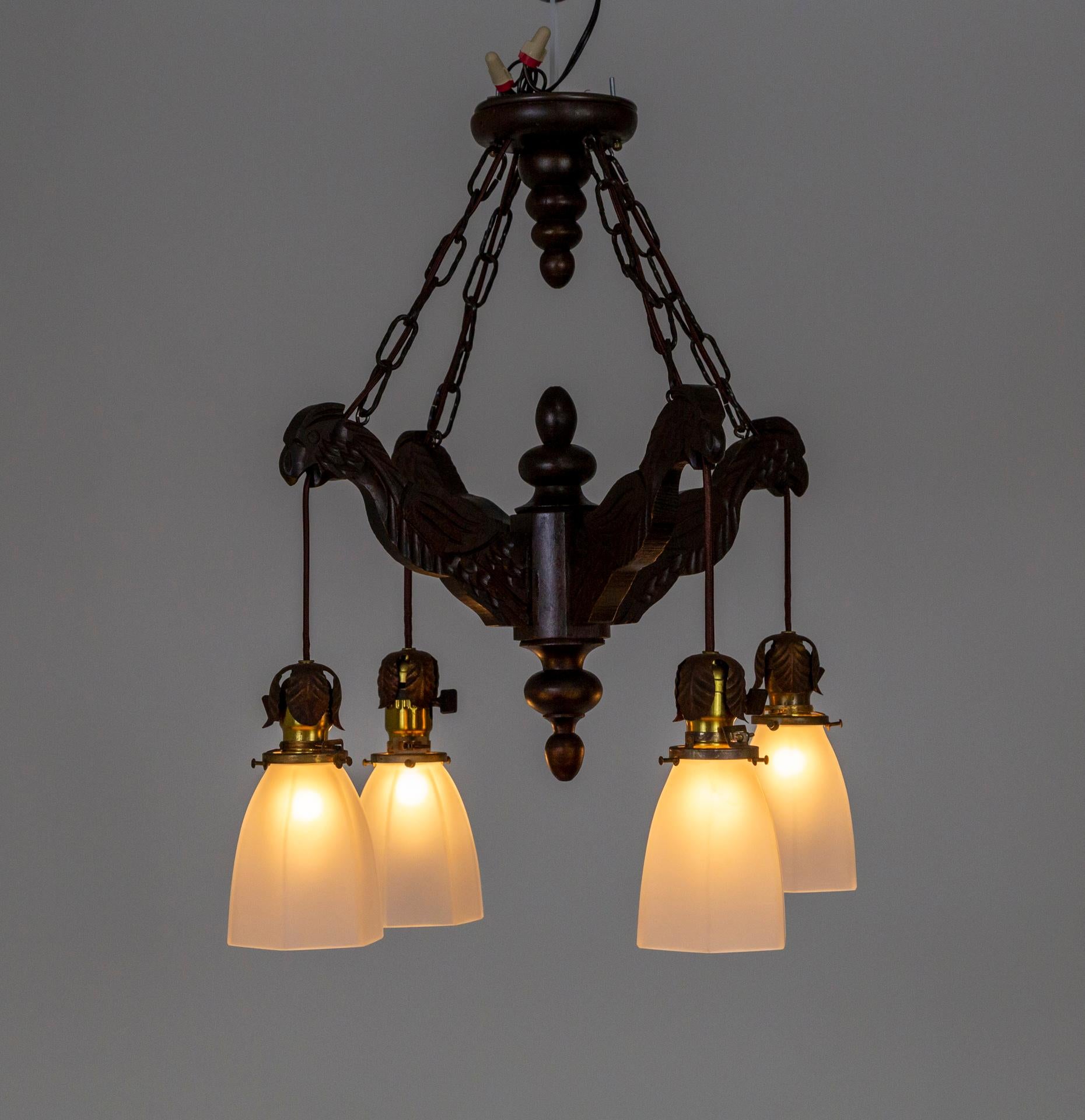 A dark walnut-stained wood chandelier in a 4-arm structure of basic, stylized, hand-carved birds that come together at the center pilaster with top and bottom turned finials. It hangs by four chains with an equally interesting canopy that mimics the