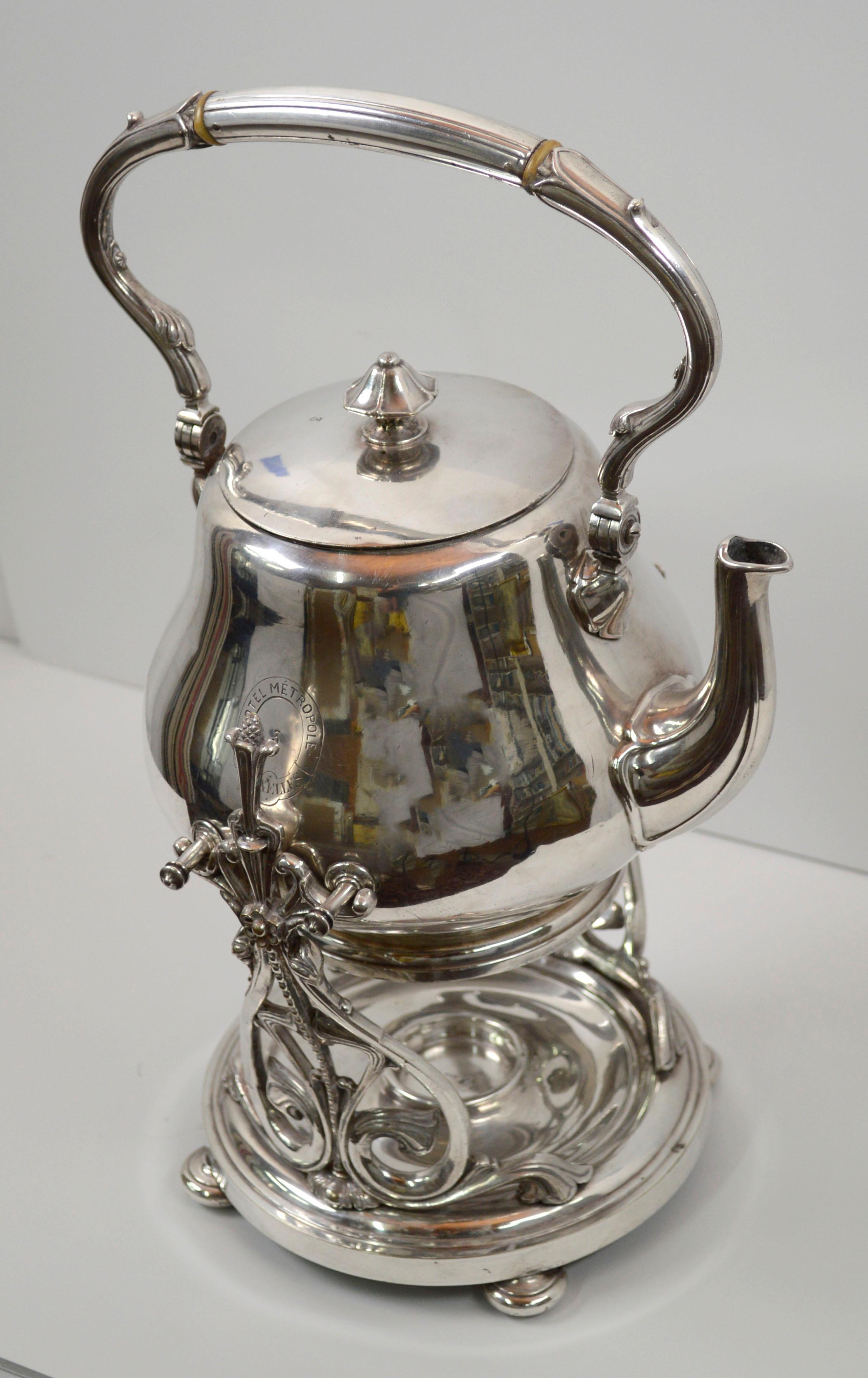 Early 20th century Hotel Metropole Brussels silver plated tilting teapot with stand, by Christofle (French, 1830-present), c.1900. Elegant floral themed filigree details decorate the handles and stand. Teapot is embossed with the logo for Hotel