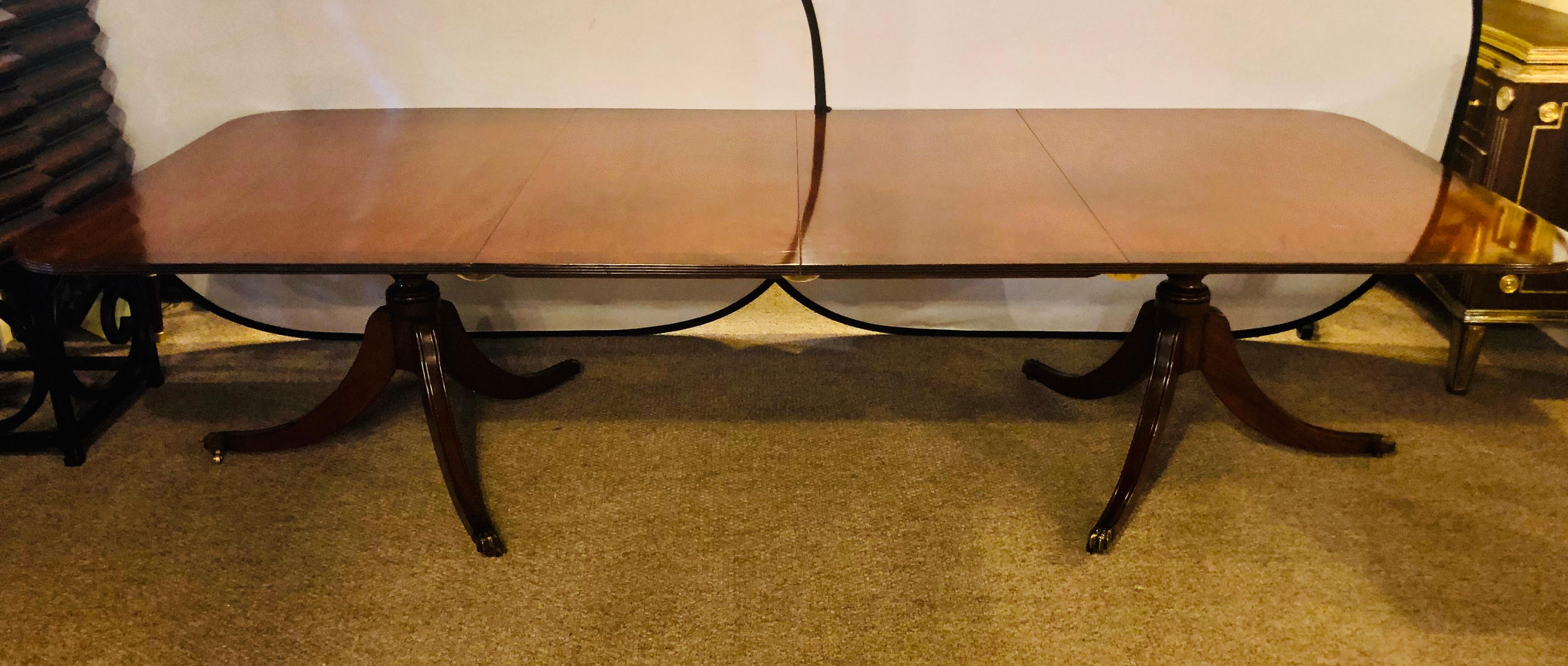 Early 20th century Georgian style banded mahogany dining table. This finely constructed dining table sits upon a tripod base double pedestal having claw brass sabots. The table has two leaves and is stationary as it will does not open and close to