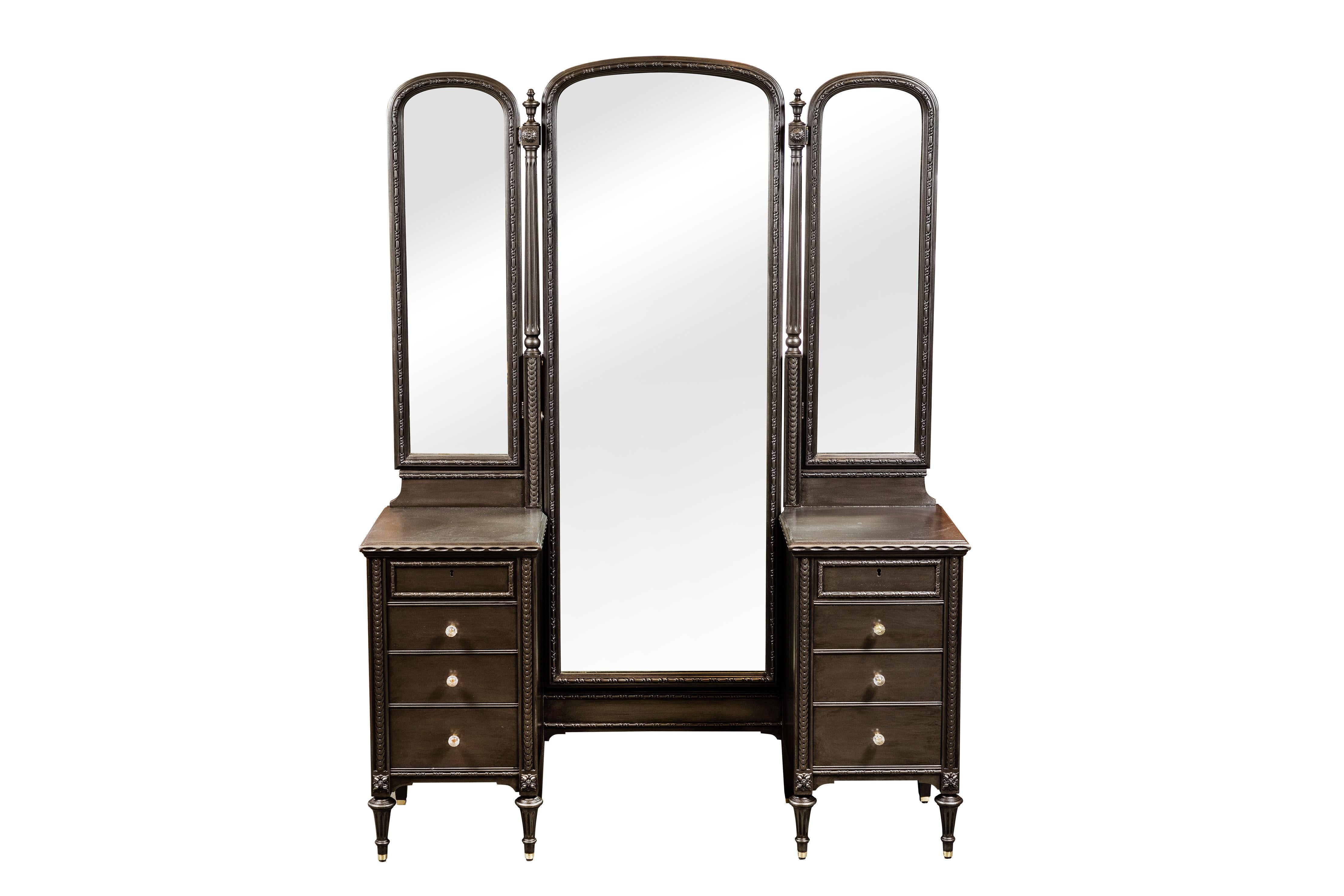 c. 1920's 3 mirror vanity.
Large center mirror tilts and 2 smaller side wing hinged mirrors can be adjusted.
Vanity has been newly painted in a metallic smoke finish and has vintage glass knobs on 6 of the 8 drawers and 2 top drawers lock with
