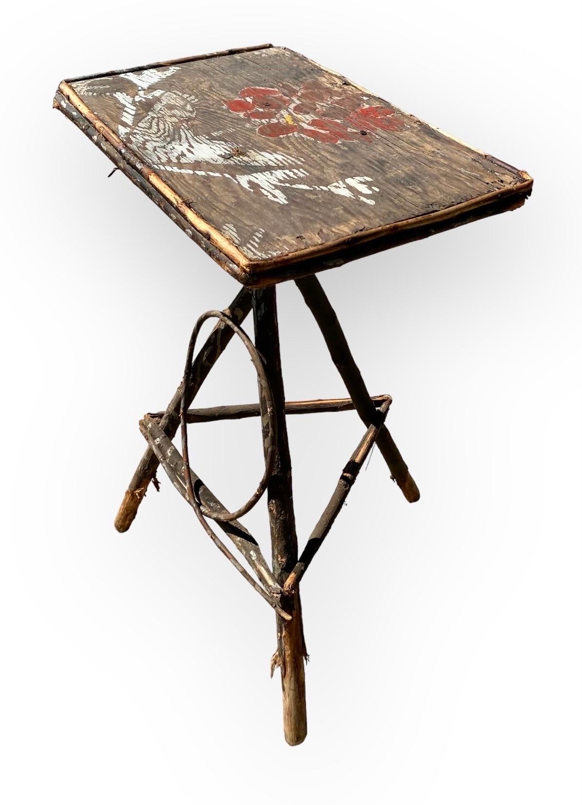 This is an original Adirondack stand or side table with a dark finish decorated with silver painted leaves and a charming aged folk art brick red bird and floral study on the top. The base has a vine and end caps on all the wood and cross hatching
