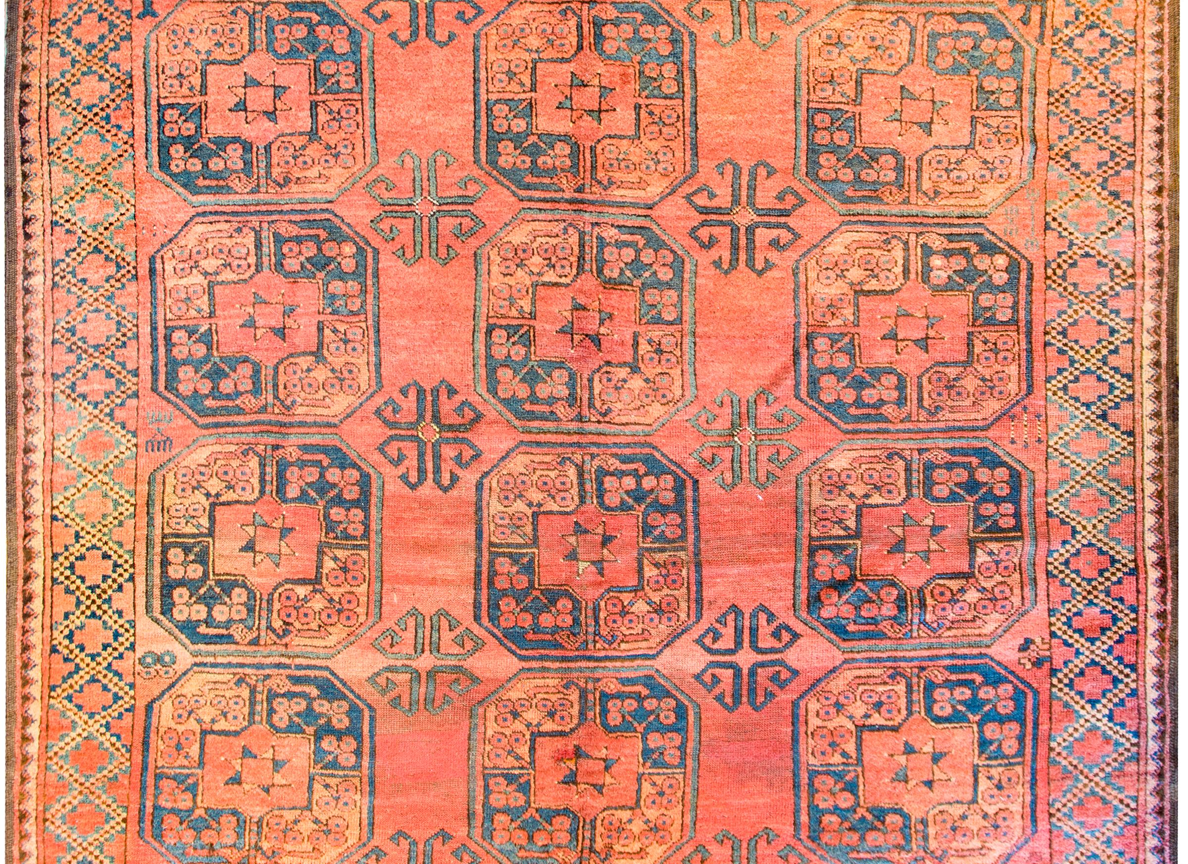An early 20th century Afghani Bashir rug with multiple large octagonal medallions woven in indigo and gold, on an orange background surrounded by a complementary geometric lattice pattern border.