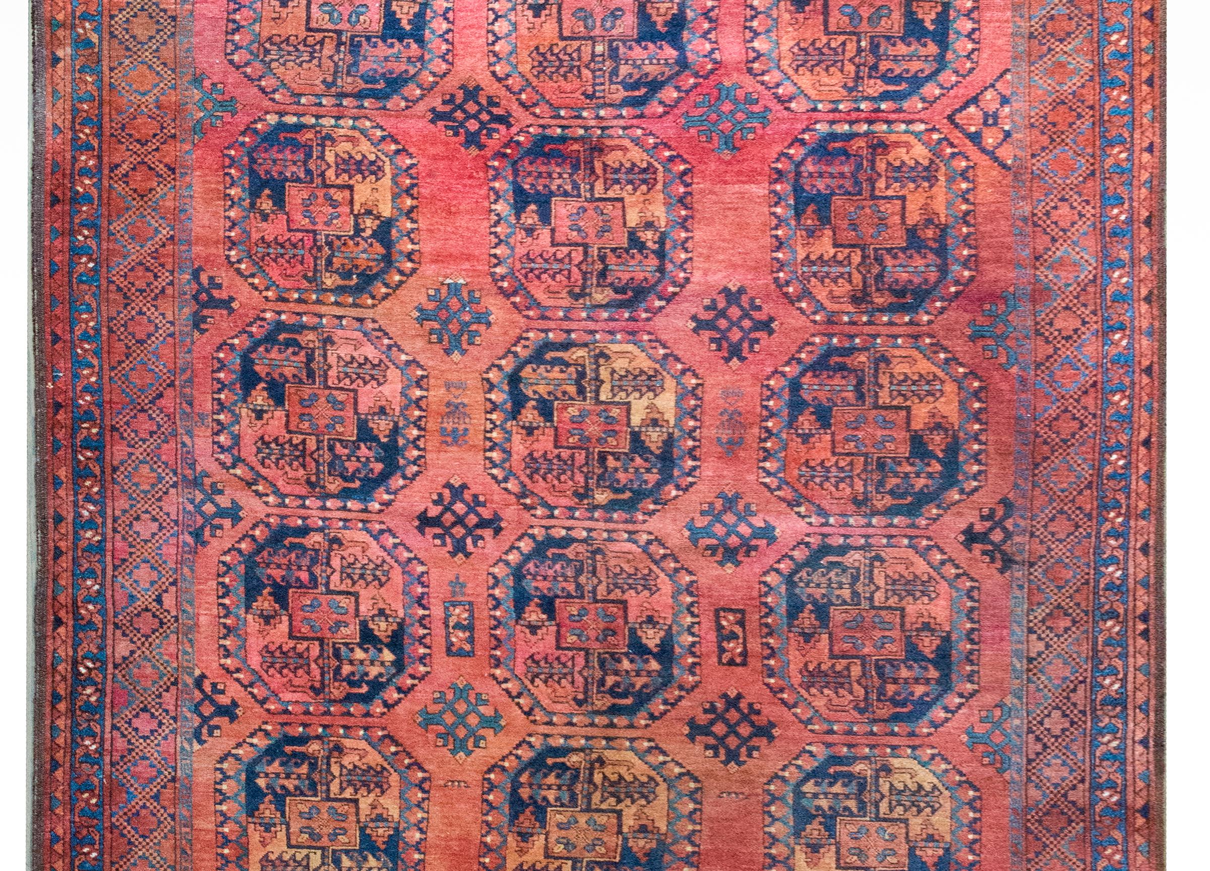 This early 20th-century Afghani Ersari rug is a striking example of tribal craftsmanship, featuring an all-over pattern of octagonal medallions, each filled with stylized floral motifs. Woven in rich shades of crimson and indigo, with accents of