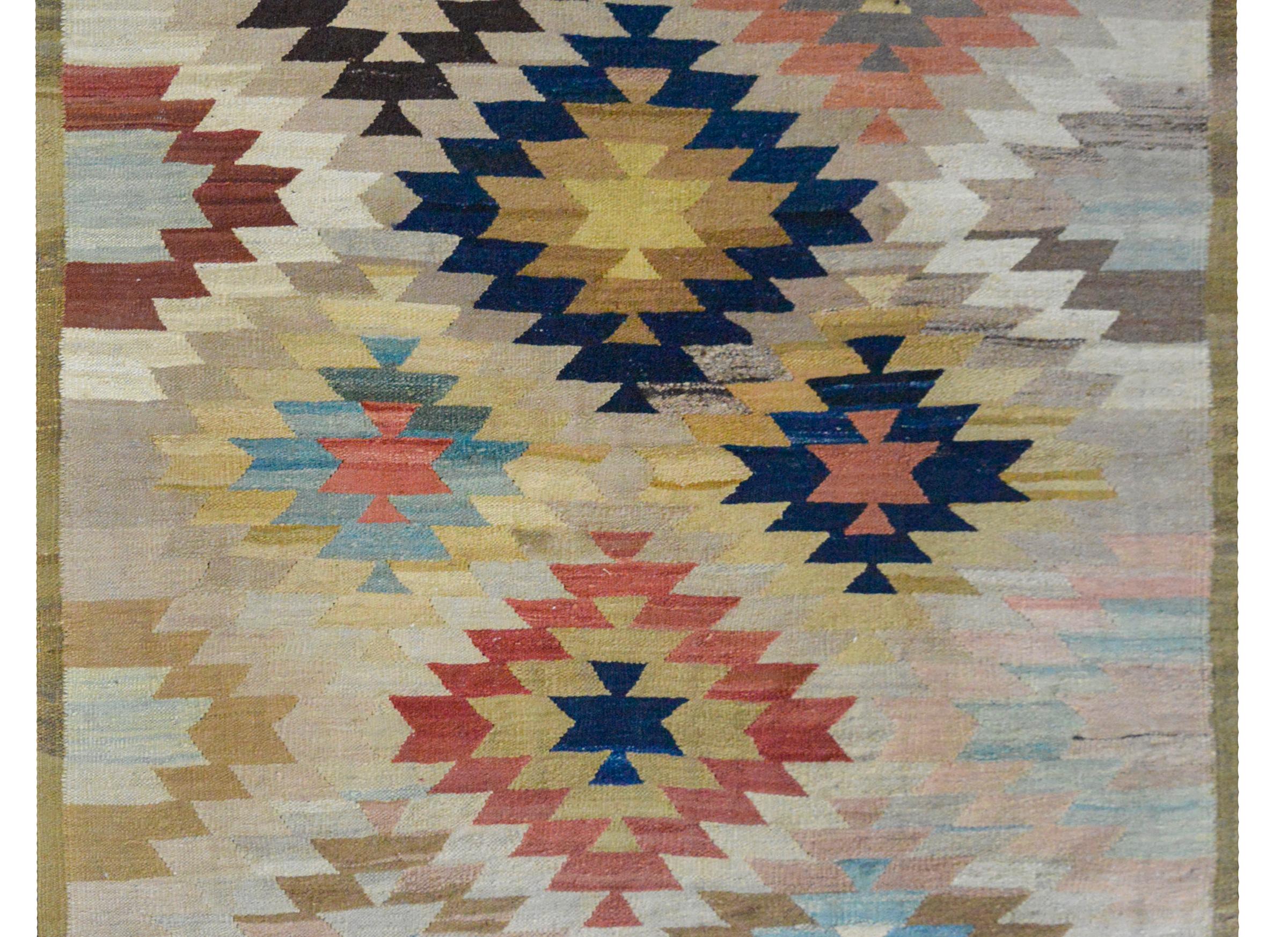 A wonderful and bold late 20th century Afghani Kilim rug with a large-scale geometric pattern woven in myriad colors including crimson, gold, pink, gray, white, and dark indigo, and surrounded by a thin striped border.