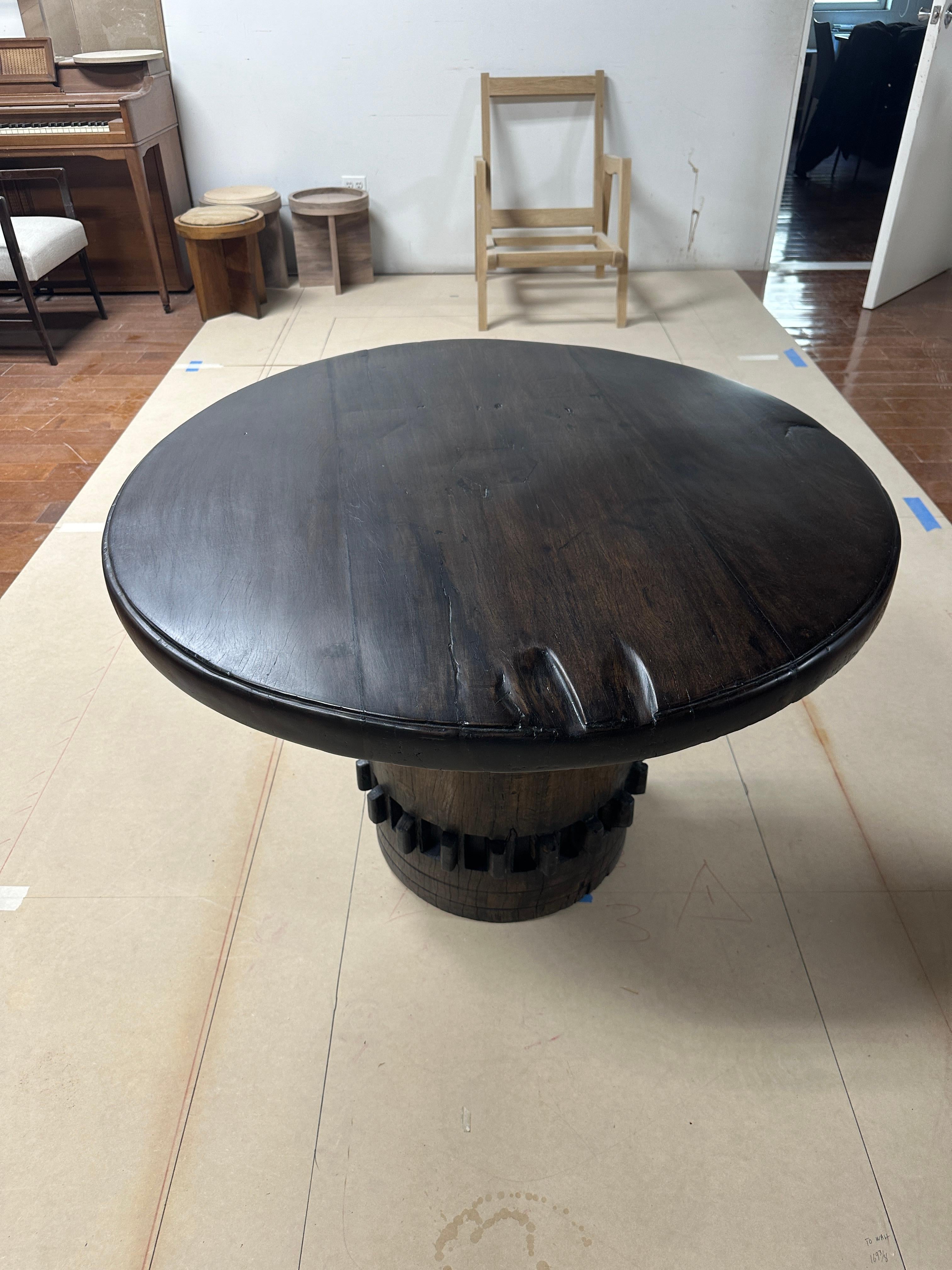 Cette table ronde en bois du début du XXe siècle est dotée d'une remarquable base de broyeur de sucre de canne africain. Cette pièce unique a été réaffectée avec soin à partir d'un outil antique utilisé autrefois pour le traitement de la canne à