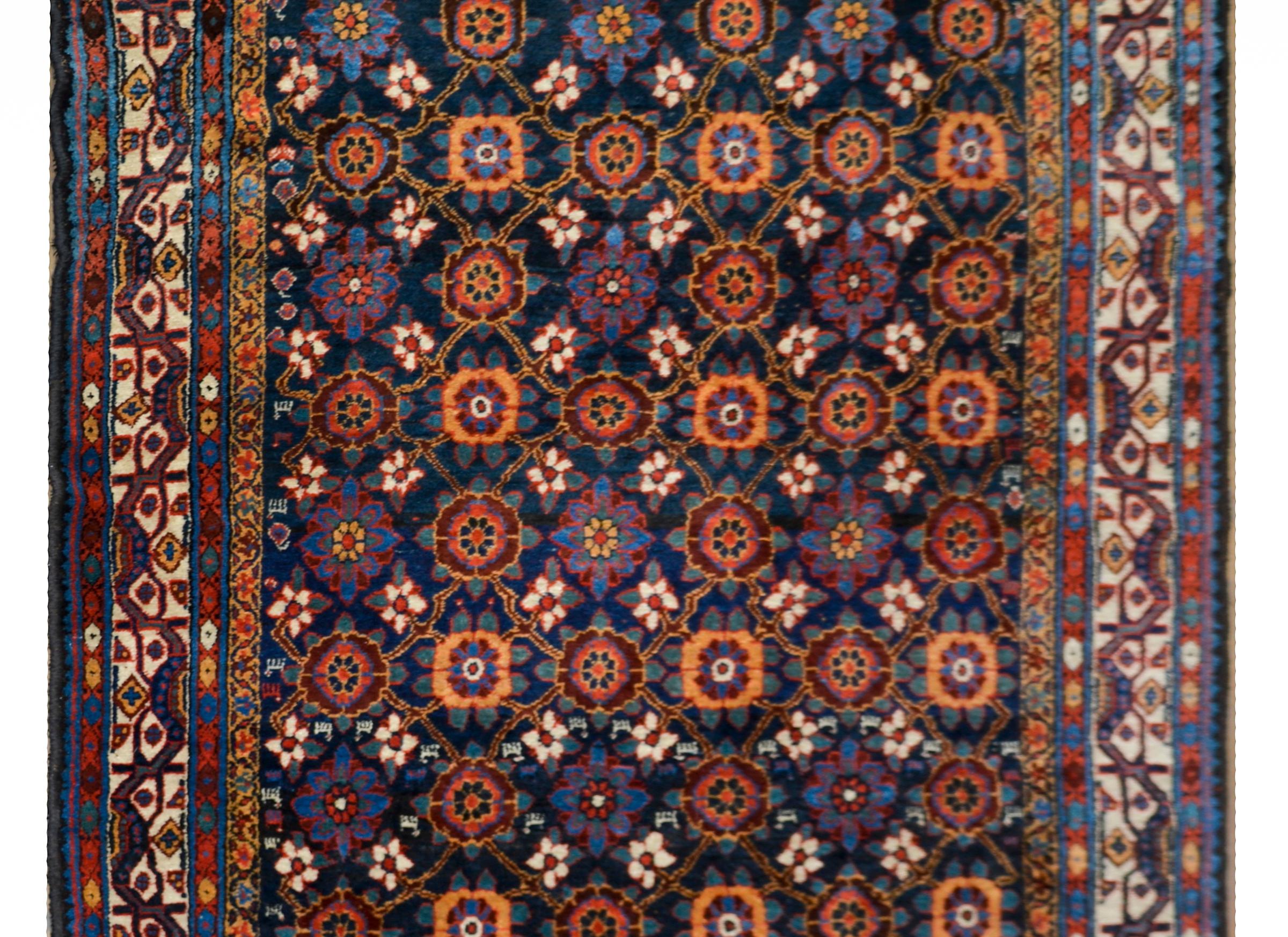 A stunning early 20th century Persian Afshar rug with an all-over floral trellis pattern woven in brilliant reds, greens, yellows, and blues, and surrounded by a wide border containing a scrolling vine pattern flanked by pairs of matching petite