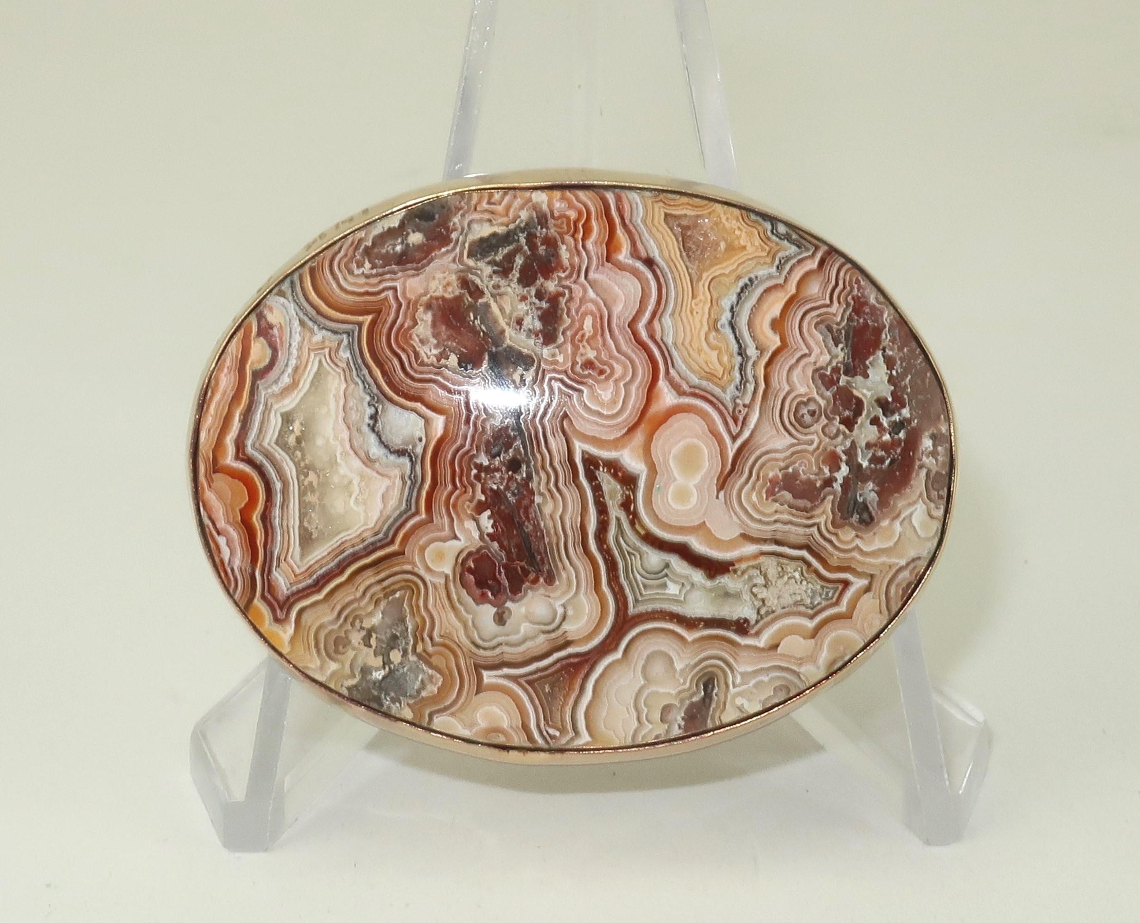 A gorgeous oval shaped polished agate framed in a 14K gold setting outfitted with straight pin hardware.  The agate is in earth tone shades of brown and amber orange.  The intricate pattern of nature’s design is known as ‘crazy lace’.  The 14K gold