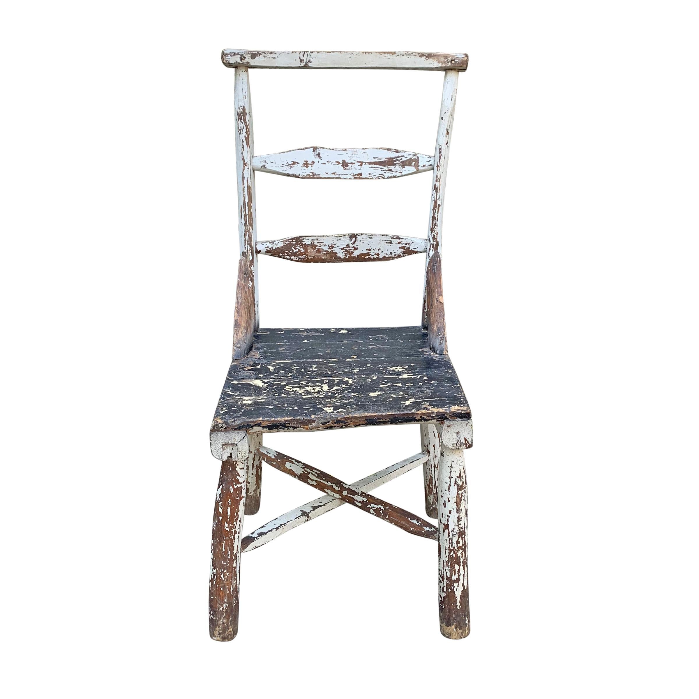 A beautiful early 20th century American Adirondack ladder-back chair of wonderful sculptural and primitive form with white and black chippy paint.