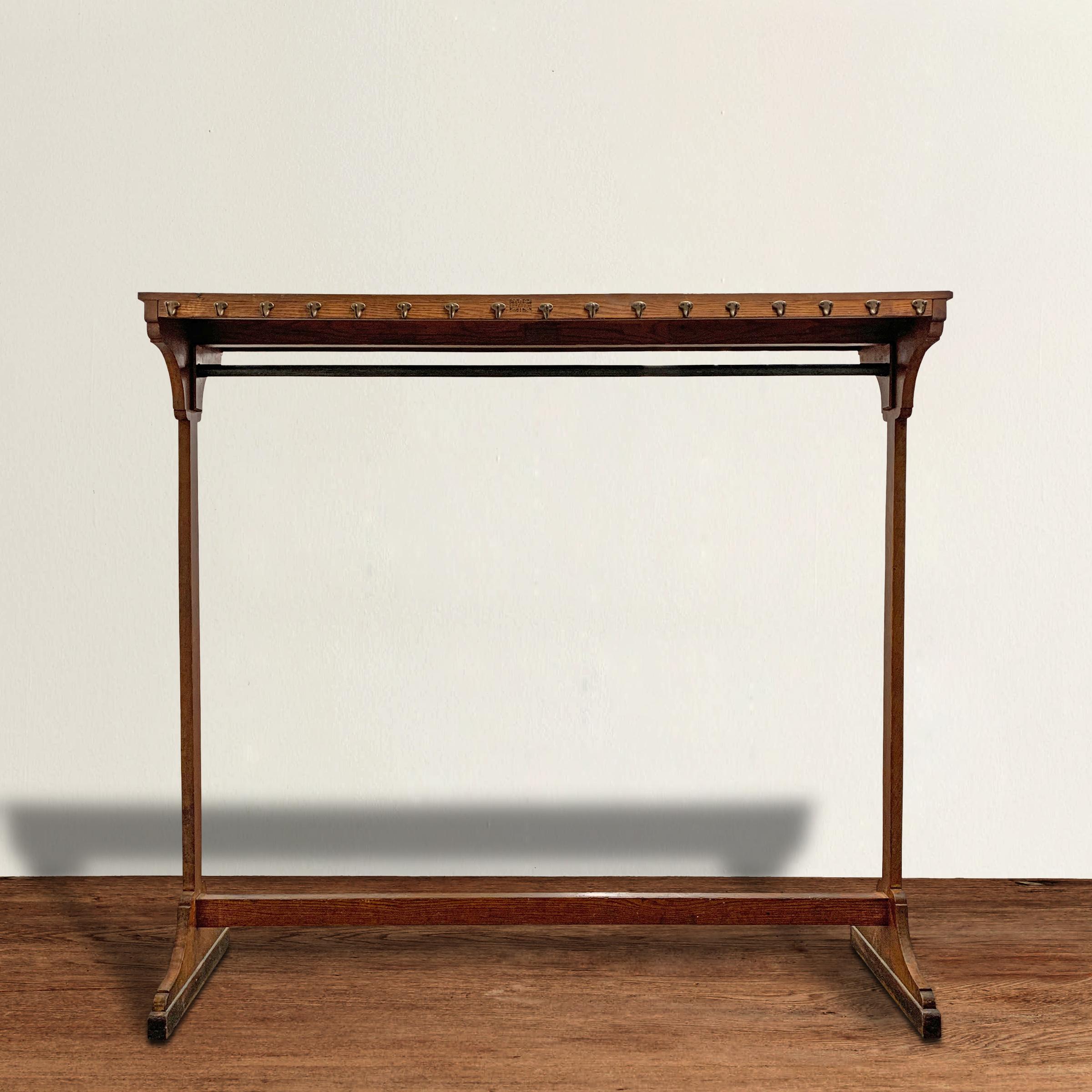 A wonderful early 20th century oak clothing rack with a top shelf, seventeen hooks on the face of the shelf, and a long rod for hangers. Excellent store fixture for a clothing boutique or alternative closet storage in a home. Marked 