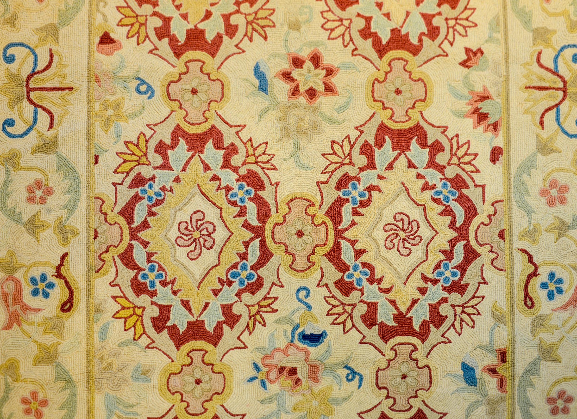 20th century Folk Art hook rug with several crimson floral medallions with stylized flowers woven in indigo, gold, cream, pink, and green on a cream colored ground. The border is similarly patterned with scrolling vines and flowers.