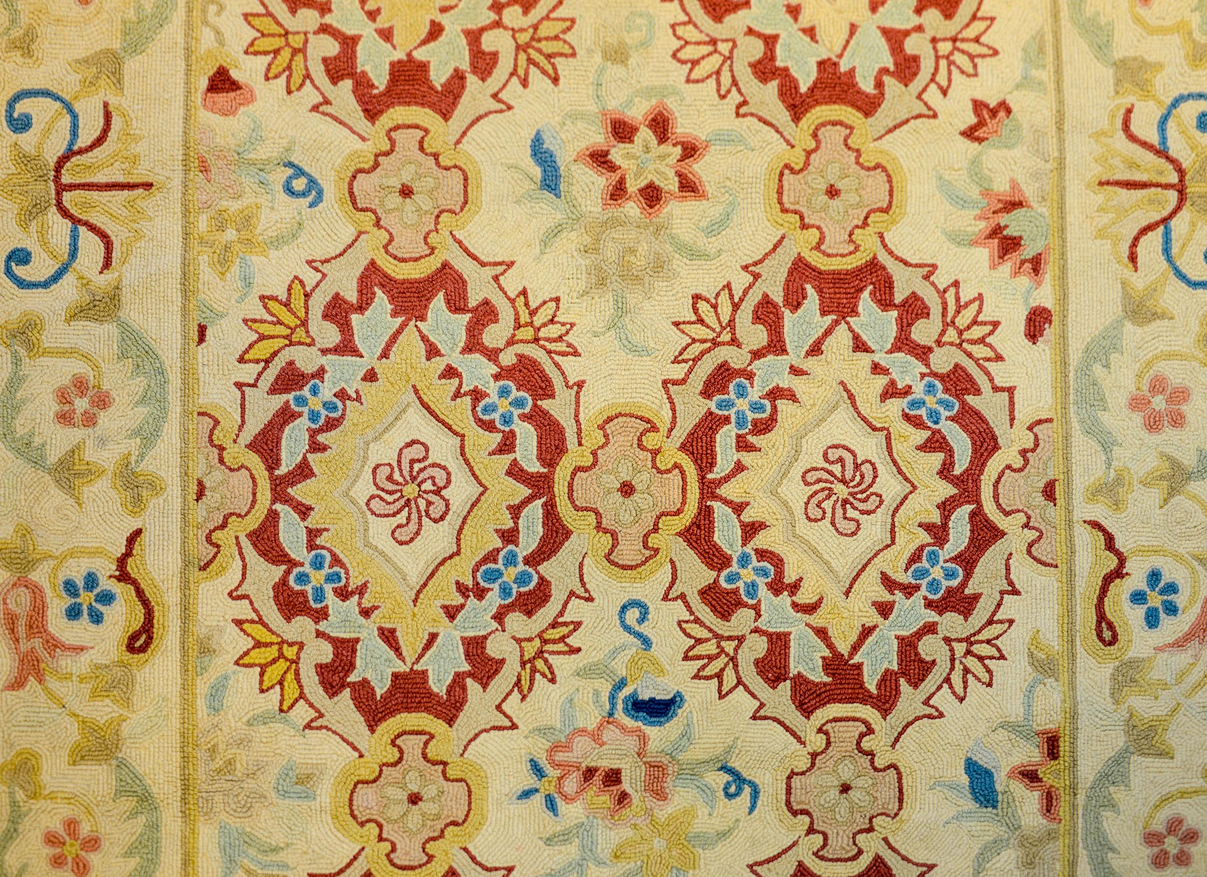 folk-Art-Hakenteppich des 20. Jahrhunderts mit mehreren karminroten Blumenmedaillons mit stilisierten Blumen, die in Indigo, Gold, Creme, Rosa und Grün auf cremefarbenem Grund gewebt sind. Die Umrandung ist in ähnlicher Weise mit Ranken und Blumen