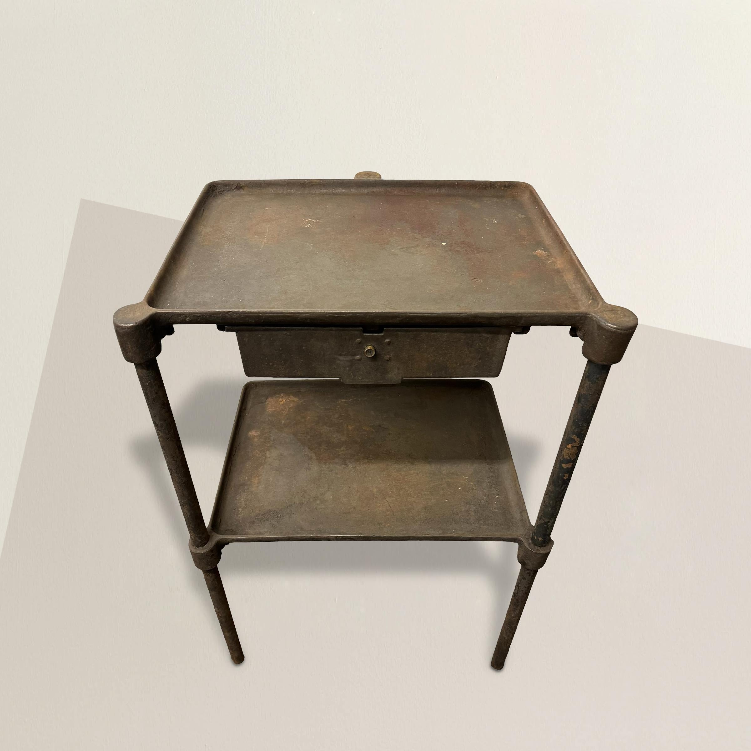 This early 20th-century American industrial steel table embodies the raw functionality and utilitarian aesthetic of industrial design. With three sturdy legs, a single drawer, and a shelf below, this table was designed for practicality rather than