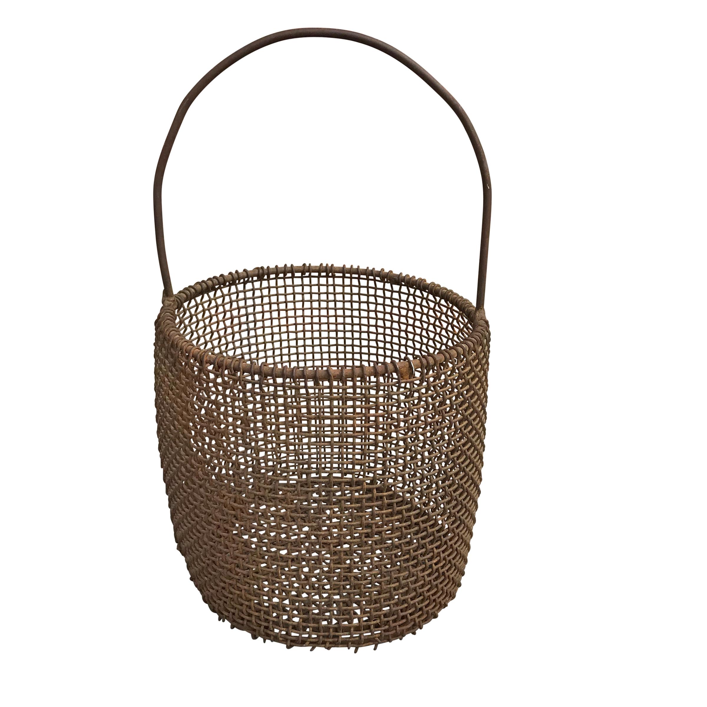 An early 20th century American industrial woven wire mesh basket with a bent iron handle, and a perfectly folksy sculptural form. Would make an excellent firewood basket, or waste bin.