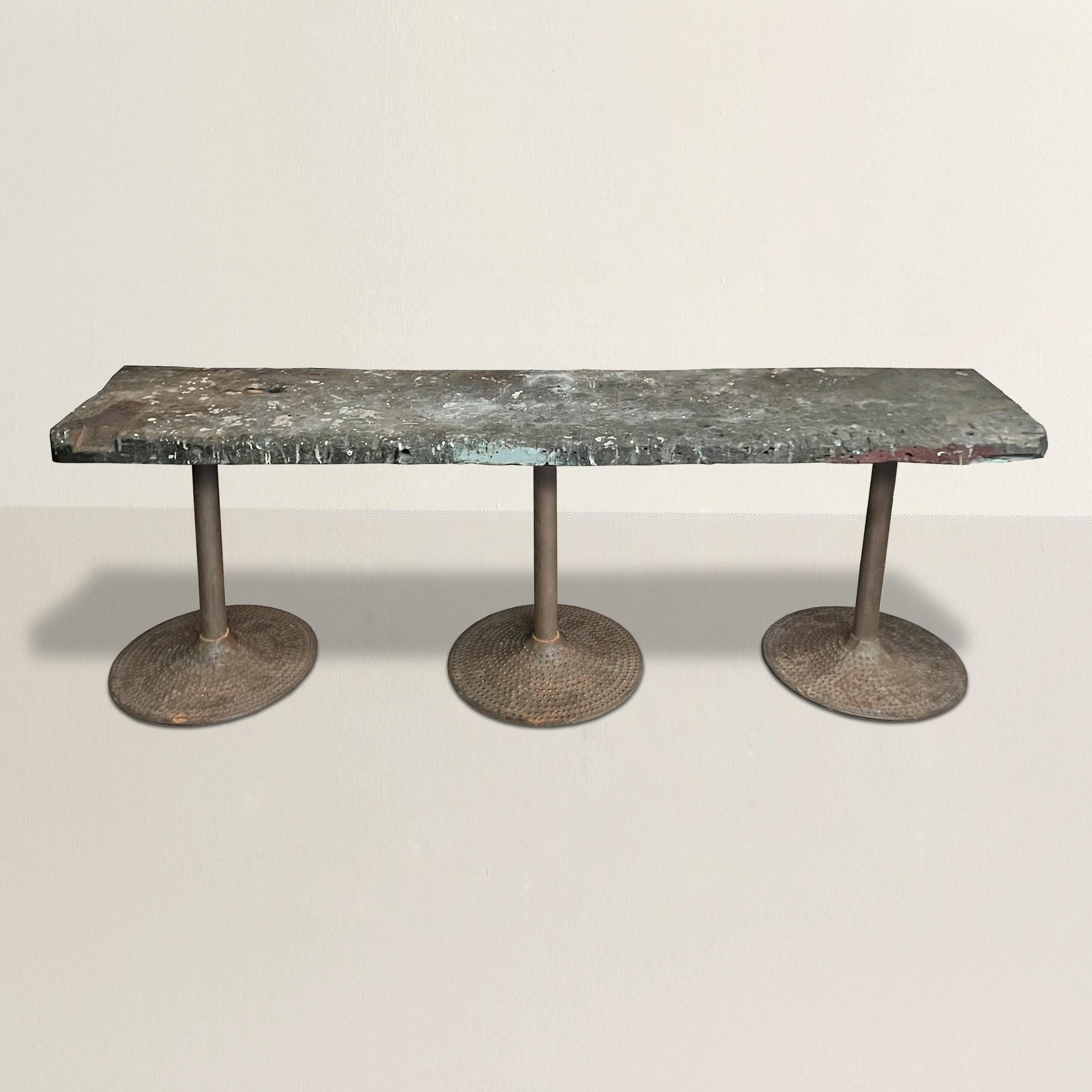 A strong and faithful early 20th century American industrial work table with the most incredible wooden top with myriad cut, saw, hammer, and paint marks from over a hundred years of use, and mounted on three cast iron pedestal legs with ribbed