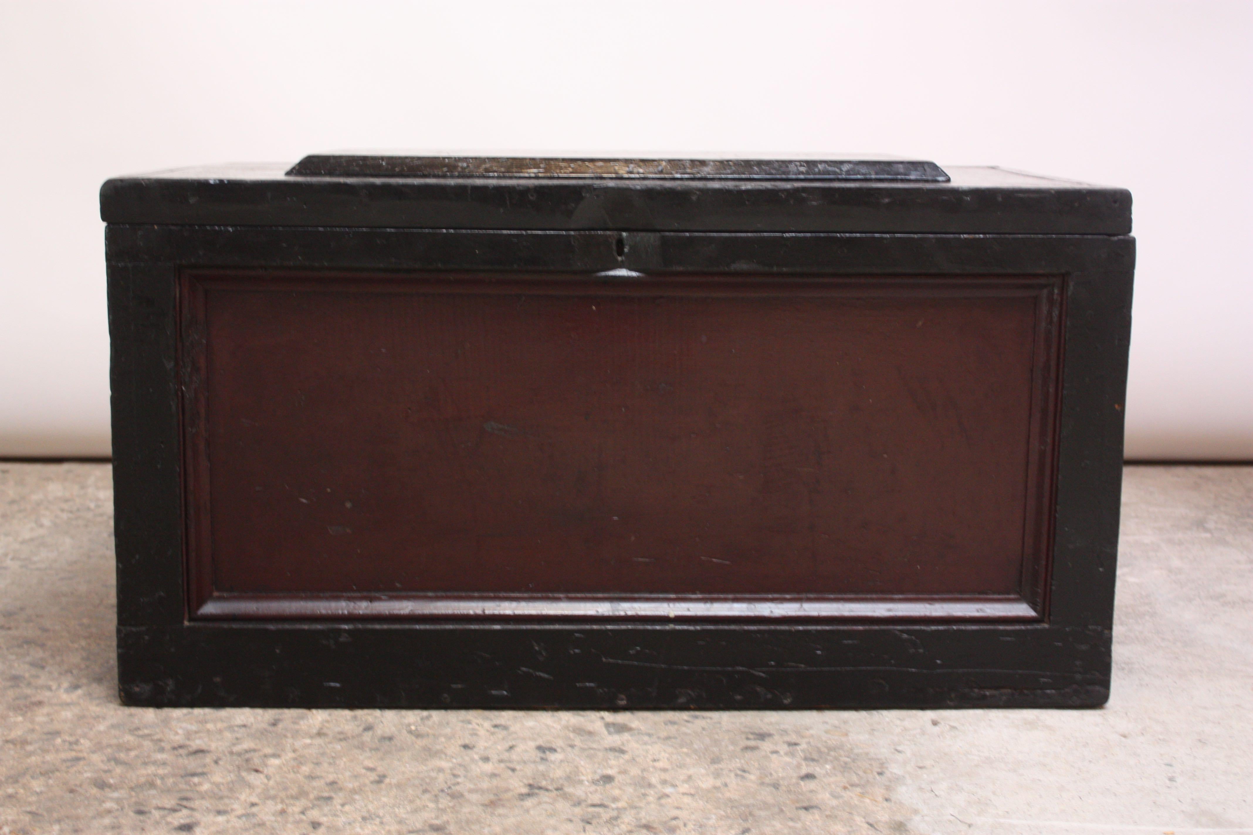 Wooden trunk / storage chest in maroon and black with a hinged top that opens to reveal three, removable boxes for storage. These boxes, vintage but later additions, can be removed for open storage. Solid brass hardware notes the date of manufacture