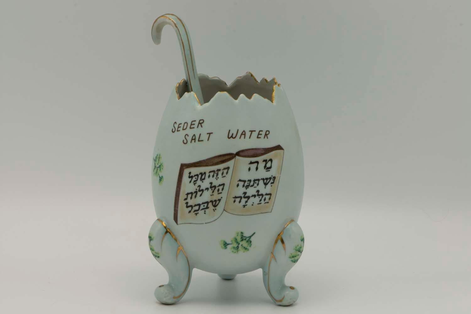 Porcelain Salt-water dish for the Passover Seder, made in the USA, circa 1910. 
Formed in the shape of a cracked egg positioned on three legs. Ornamentations in color on the dish and inscriptions in Yiddish, Hebrew and English. By an illustration of