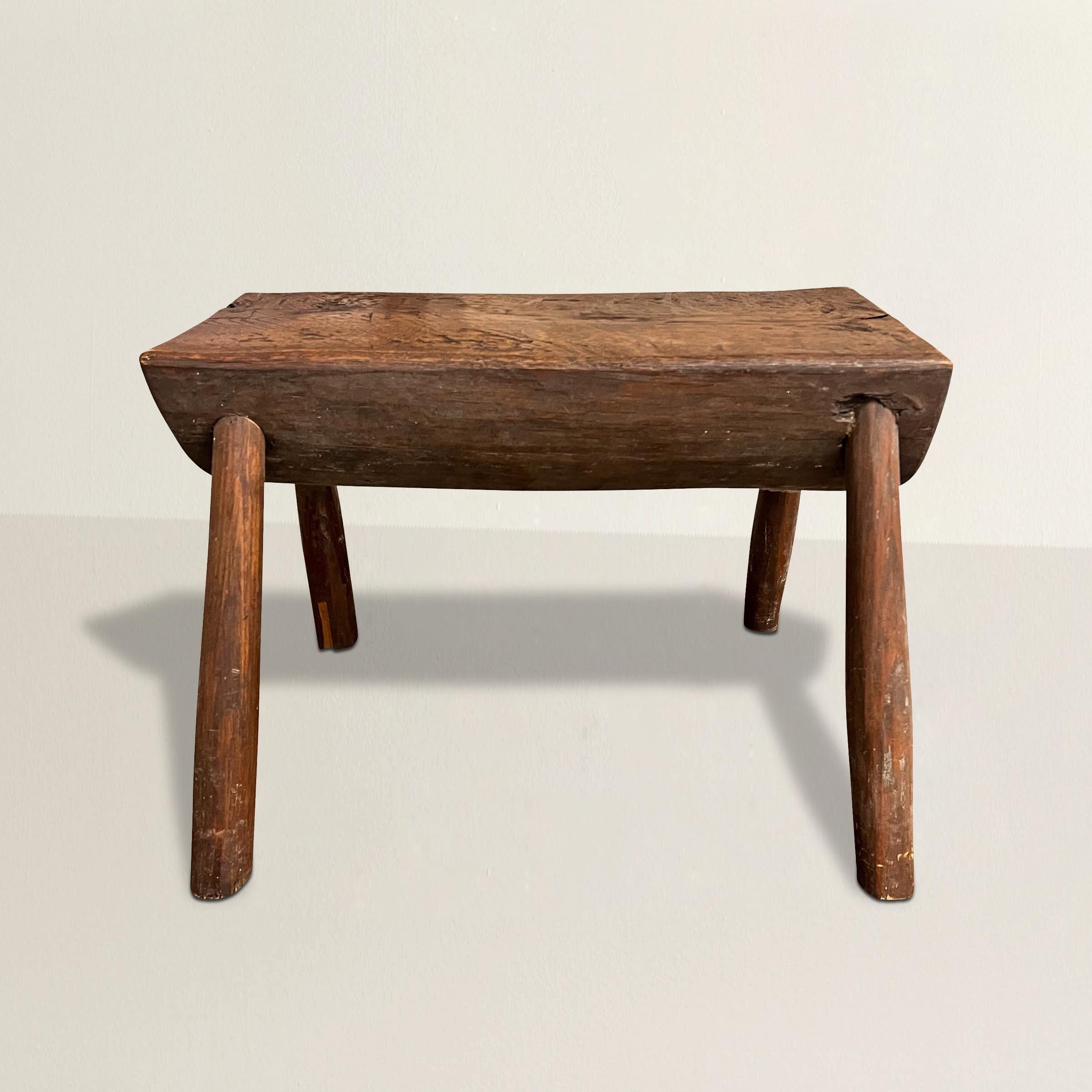 This early 20th century American primitive milking stool, with its rustic charm, embodies the essence of simplicity and ingenuity. Crafted from half of a log and supported by four skillfully whittled wood legs, this humble piece evokes a sense of
