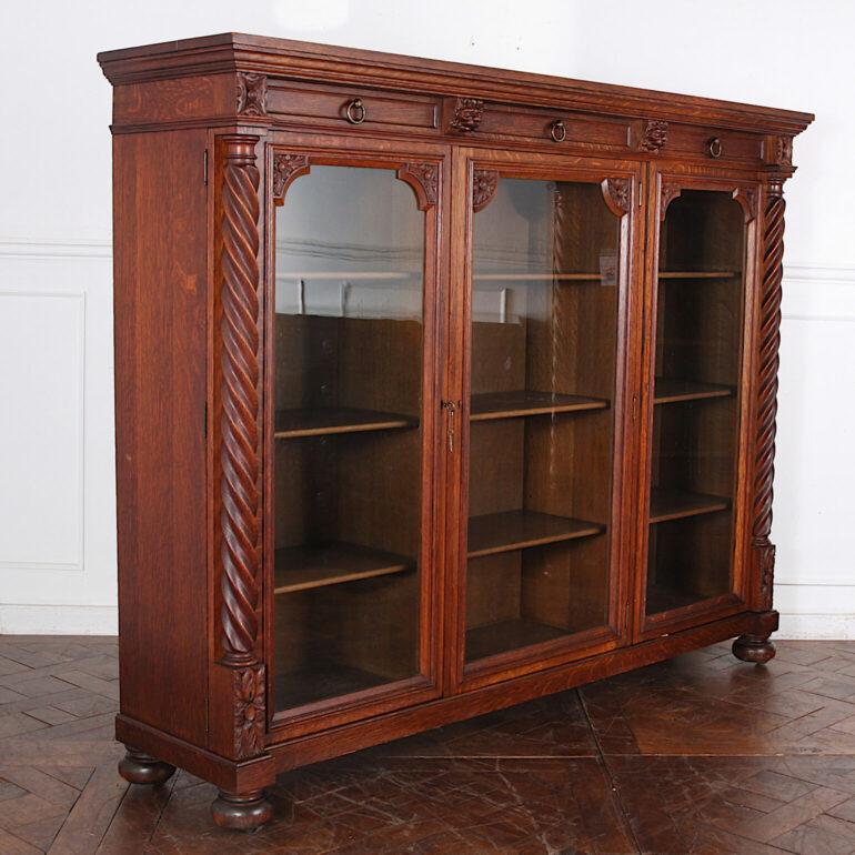 Top quality American-made solid oak bookcase with three carved doors opening to adjustable shelves and with spiral turned accent columns to each side. Three drawers fitted above the doors with original brass ring pulls, and with two ‘secret’ little